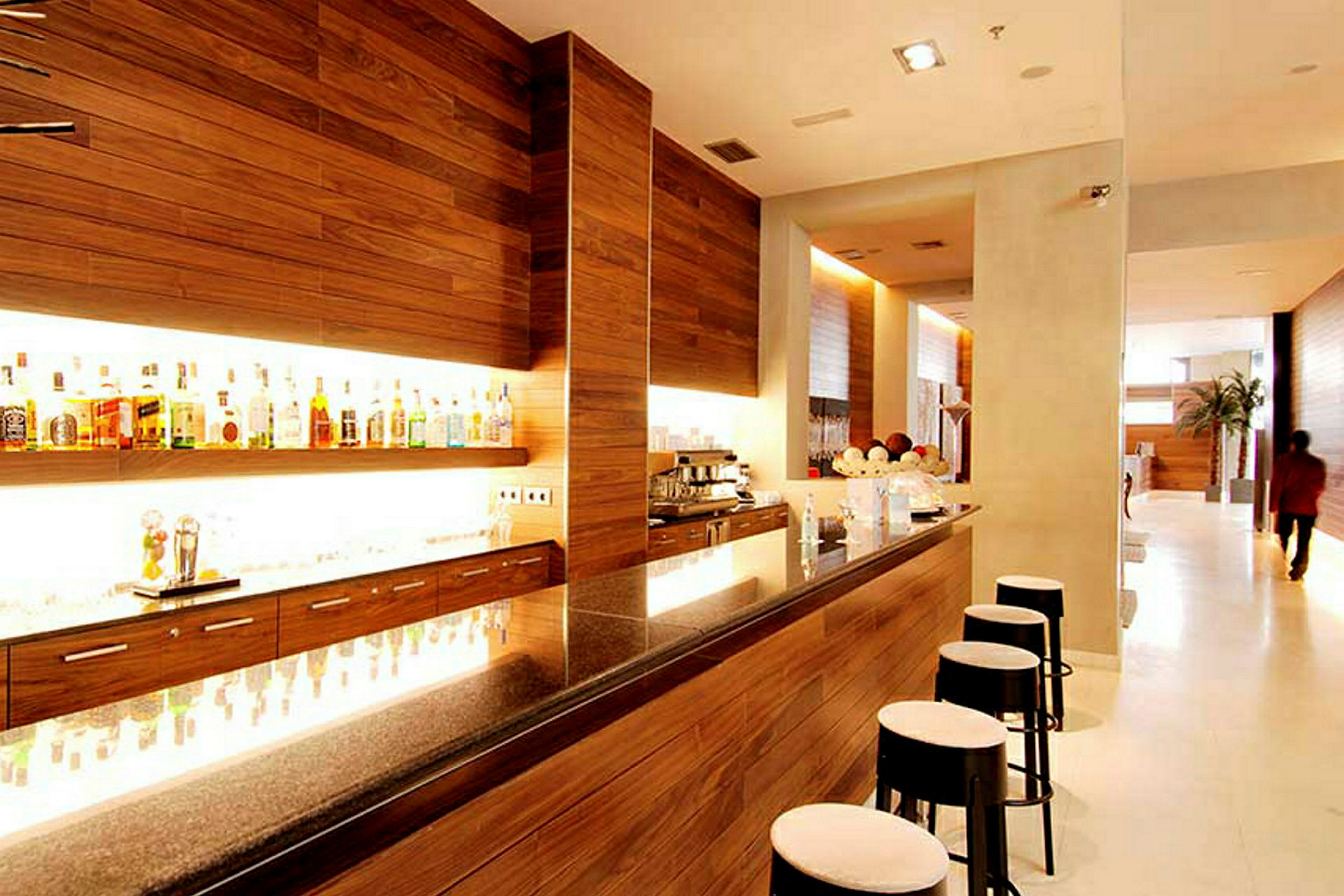 En elegant bar med träpaneler, upplyst hylla med alkoholflaskor och moderna barstolar. (AI-genererad text)