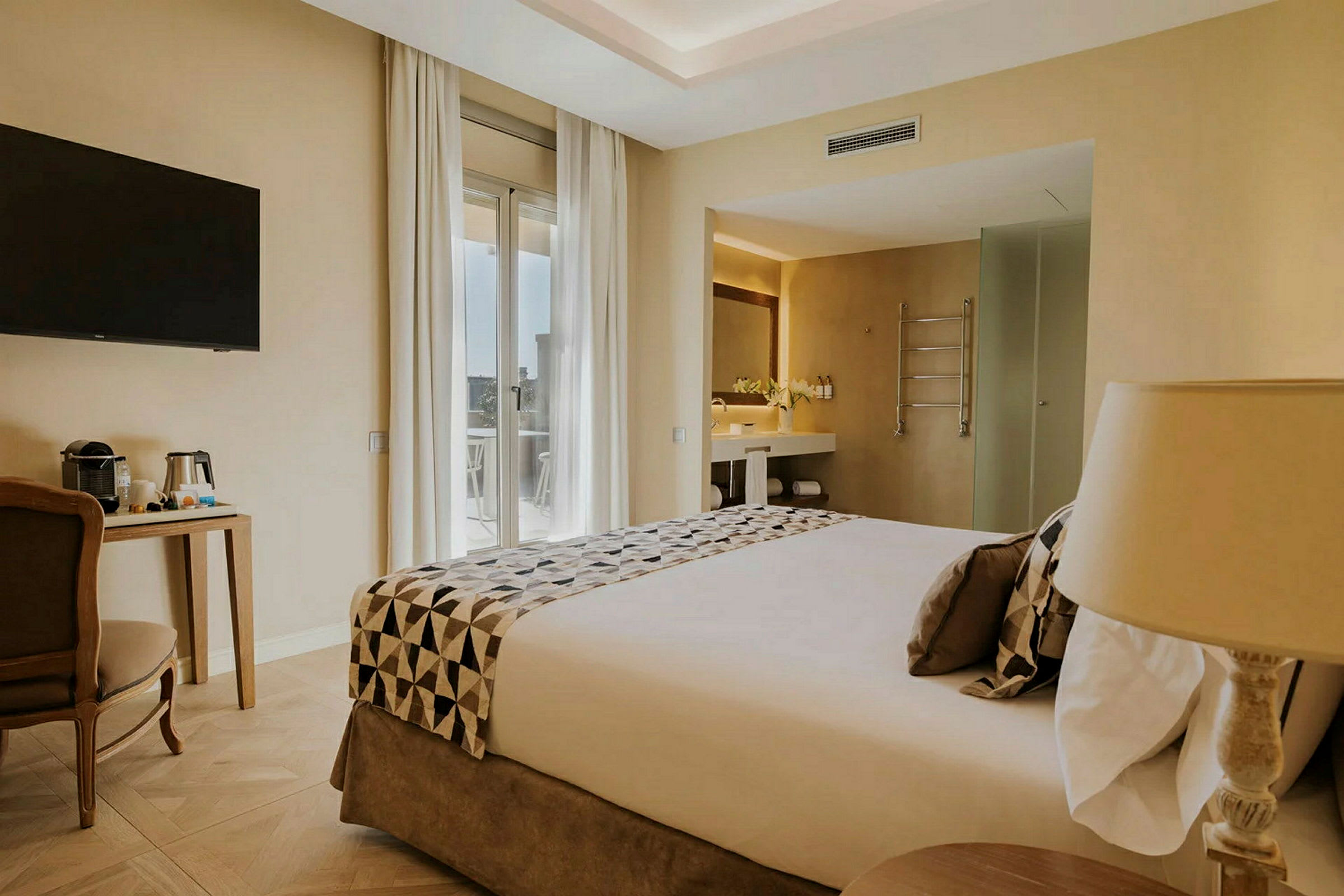 Inredningen i ett hotellrum med en bäddad dubbelsäng, en arbetsstation, en tv på väggen samt ett badrum synligt. (AI-genererad text)