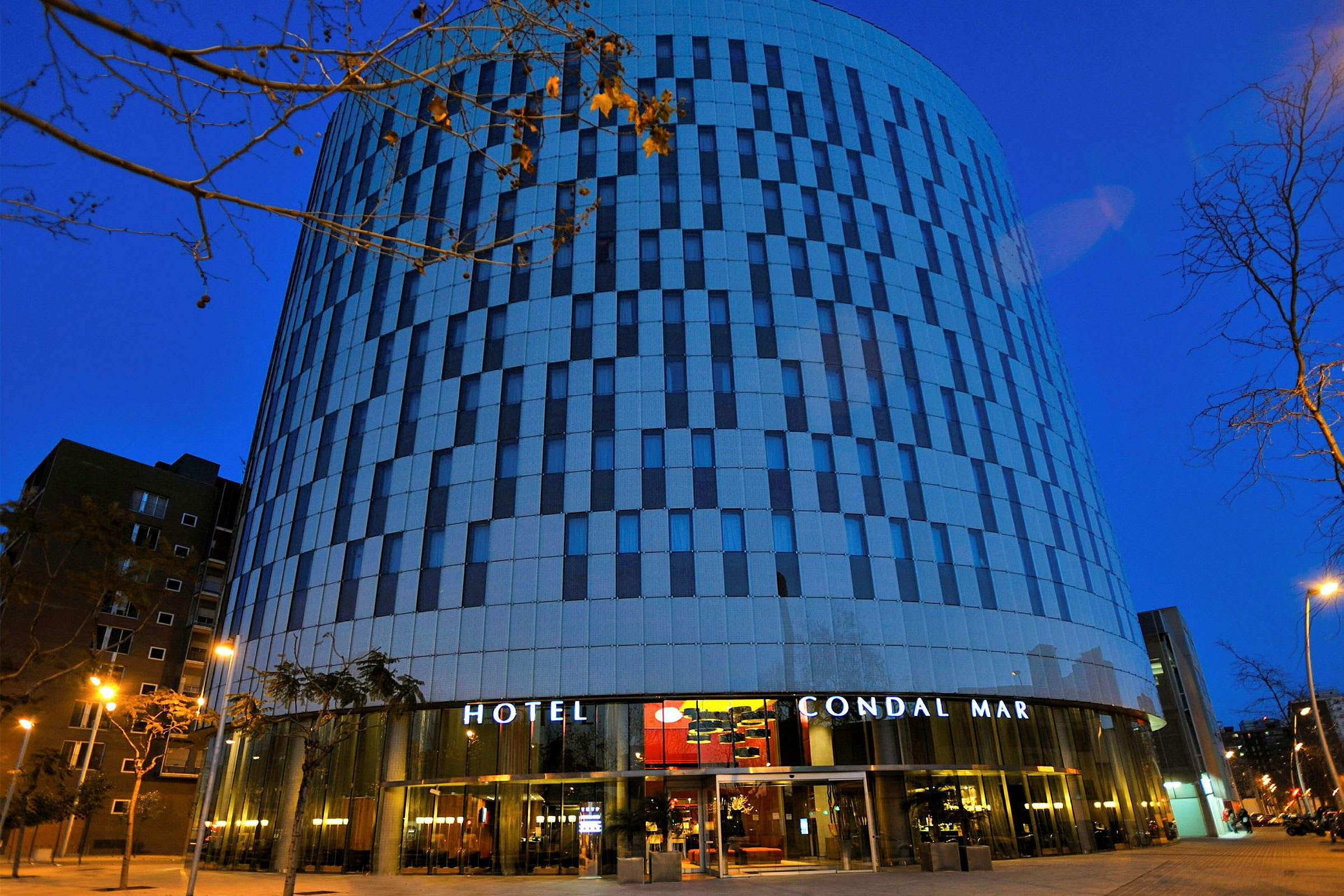 Ett hotell med modern arkitektur och fasad i ränder av glas och betong fotograferat i skymningen. (AI-genererad text)