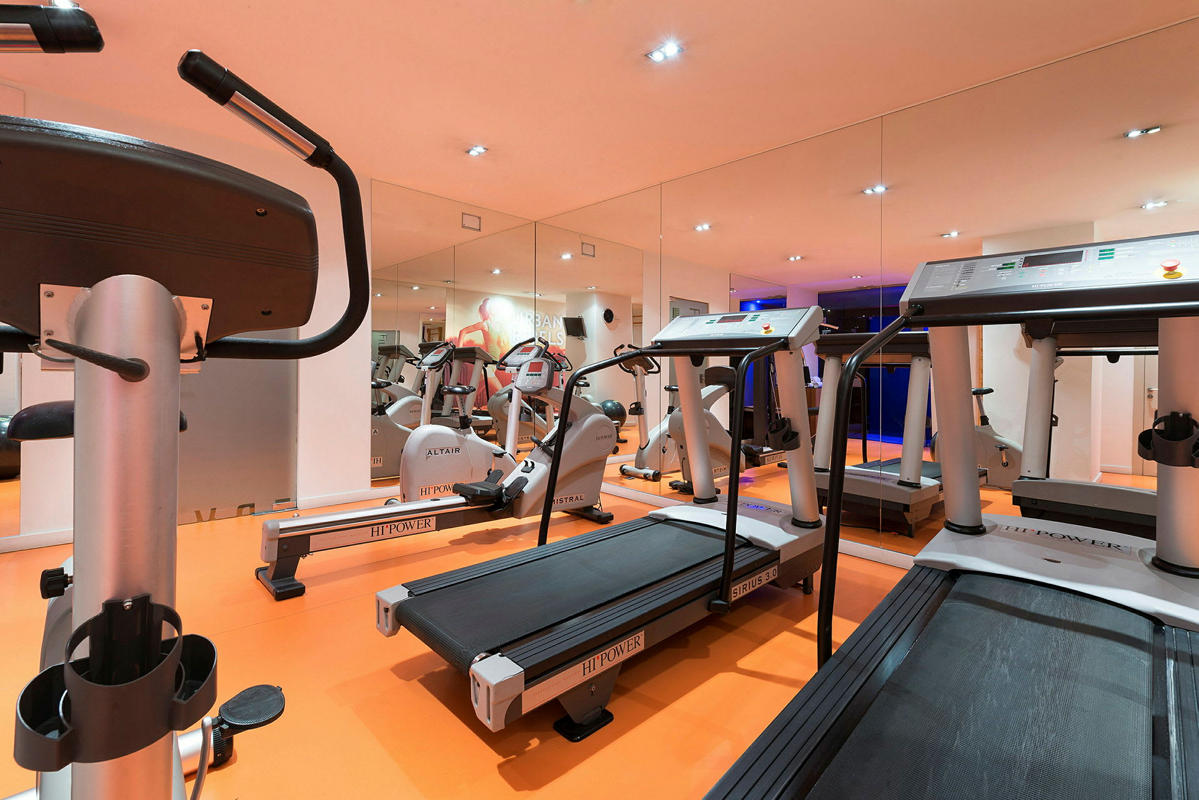Ett gym med träningsmaskiner, inklusive löpband och motionscyklar. Väggarna har speglar. (AI-genererad text)