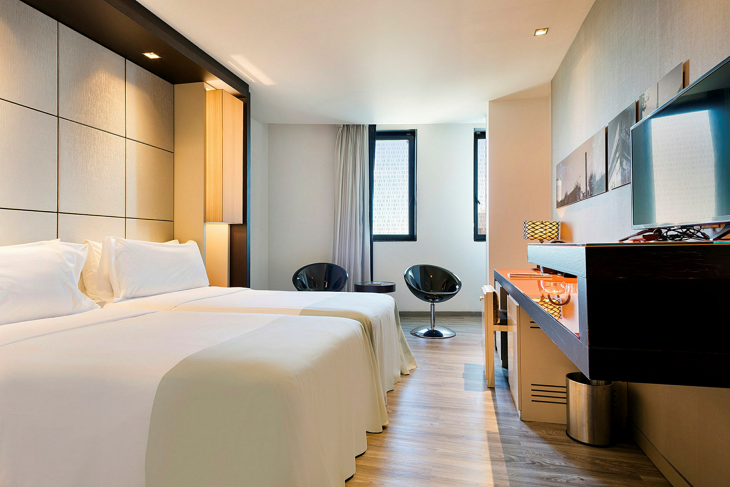Ett modernt hotellrum med två enkelsängar, liten sittgrupp och skrivbord. (AI-genererad text)