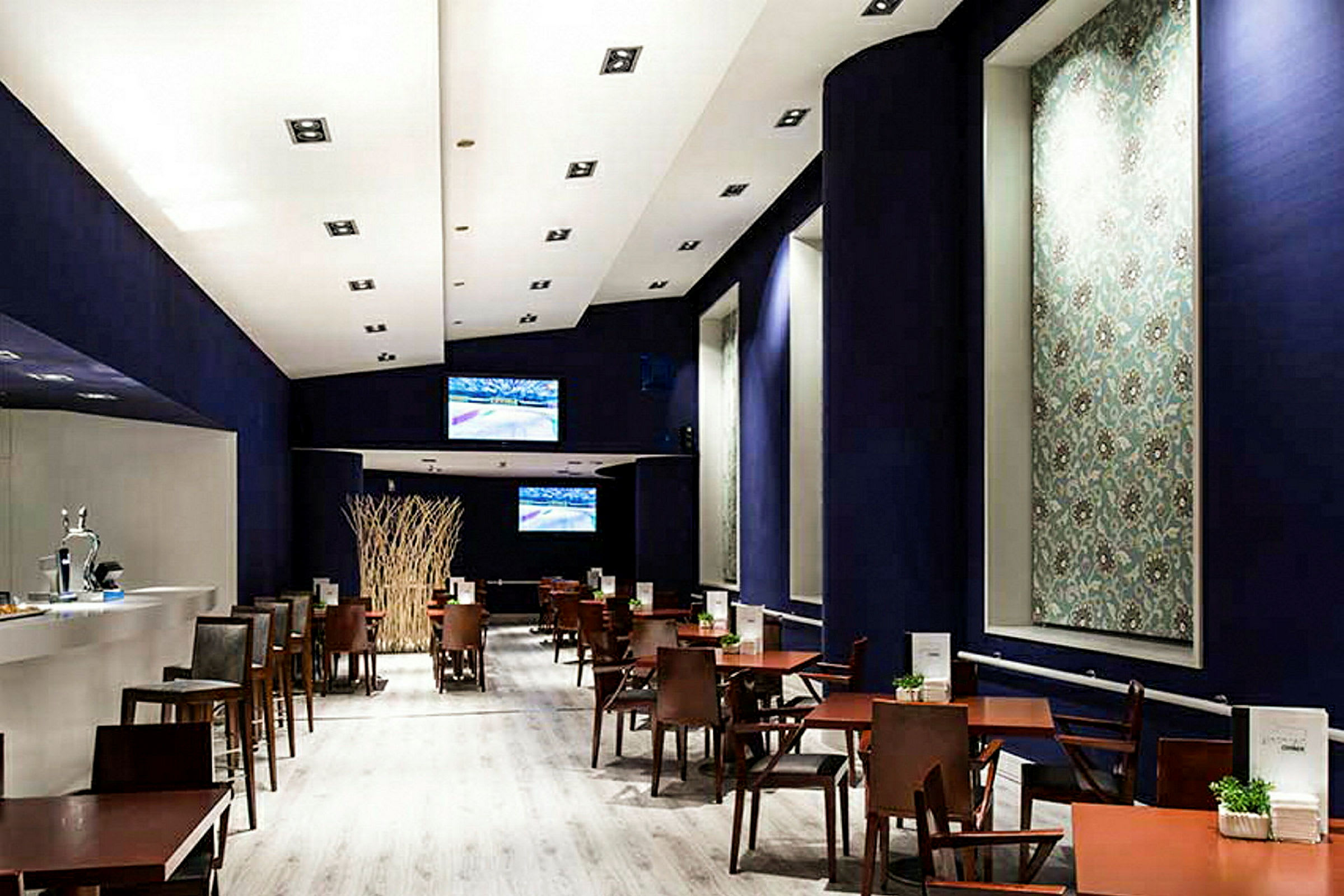 En modern restaurang eller café med trämöbler och mörk dekor. Det visar bord och stolar arrangerade i rader under ett starkt upplyst tak. (AI-genererad text)