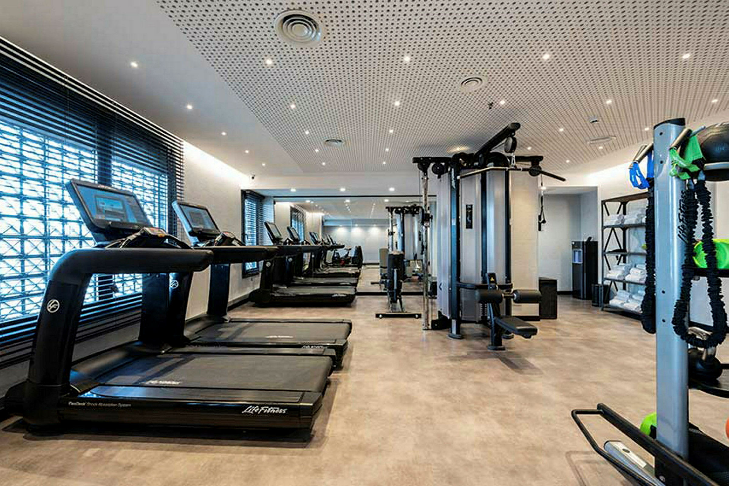 Bild av ett gym med löpband, träningsmaskiner och hyllor med handdukar. (AI-genererad text)