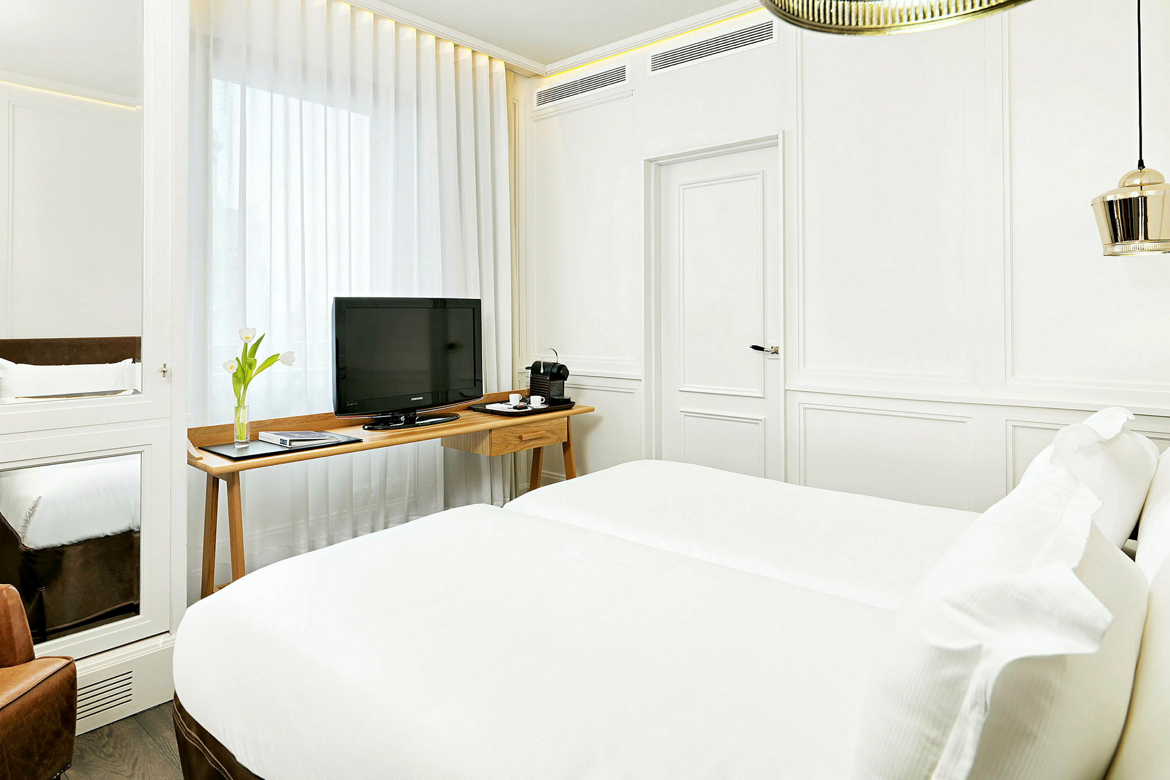 Ett ljust inrett hotellrum med vit färgsättning, en dubbelsäng, en TV på ett träbord och en kaffemaskin. (AI-genererad text)