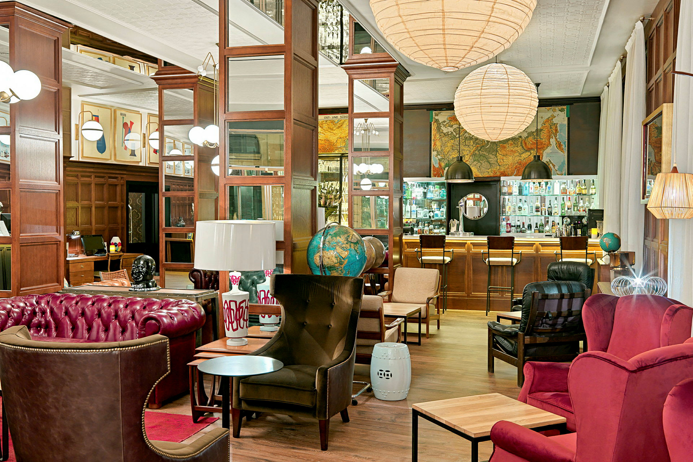 En stilfull lounge med röda och bruna möbler, glober, konstverk på väggarna och en bar med skyltdisk i bakgrunden. (AI-genererad text)