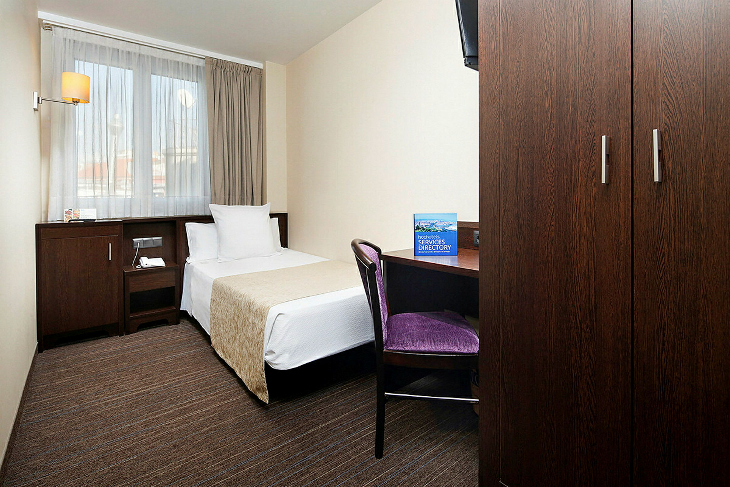 Ett hotellrum med en enkelsäng, skrivbord, stol och garderob. (AI-genererad text)