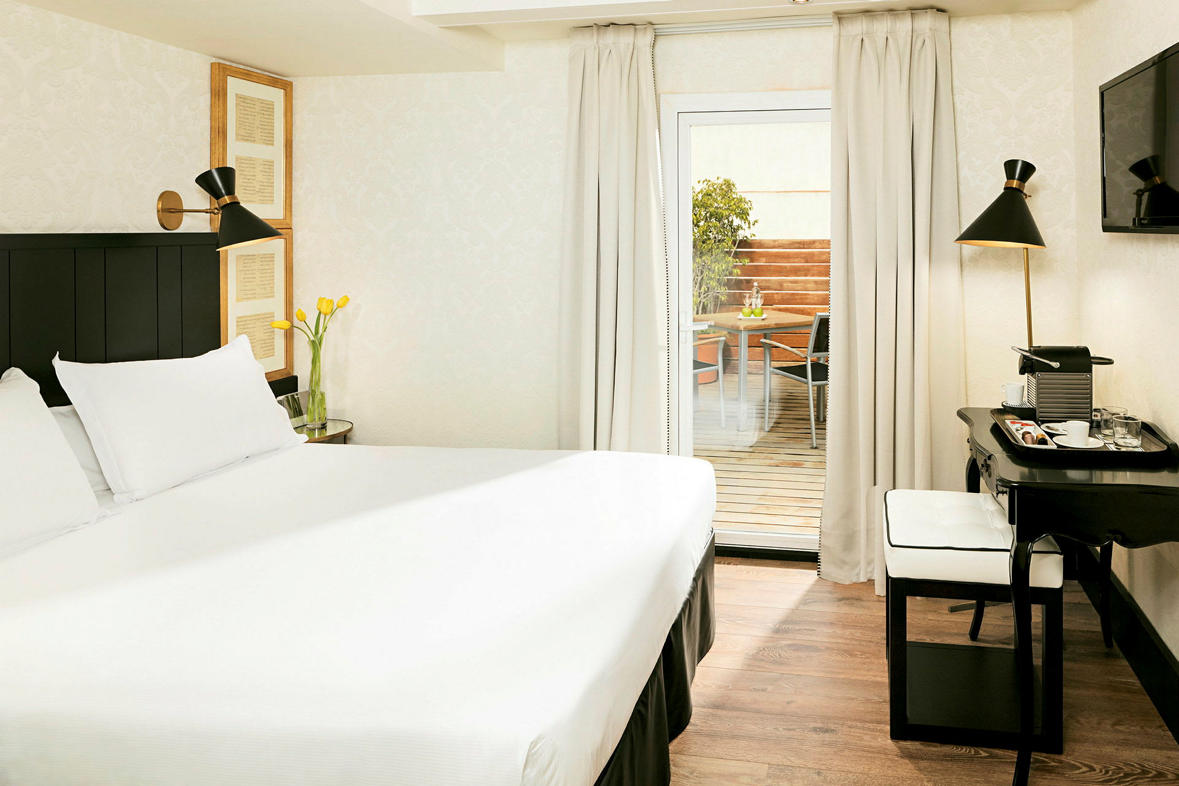 Ett hotellrum med en stor säng, vita väggar och en terrass som syns genom en glasdörr. På terrassen finns en sittgrupp. (AI-genererad text)