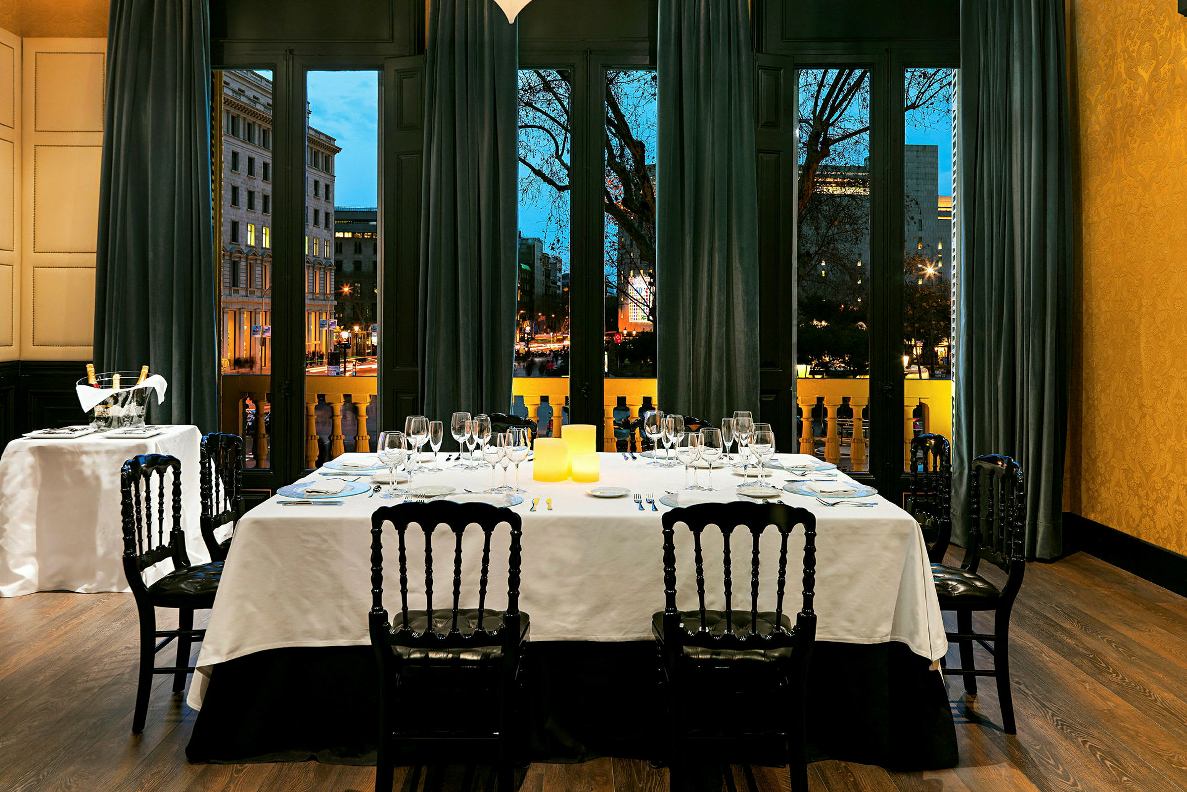 Ett elegant dukat bord i en fin restaurang med utsikt genom stora fönster mot en stadsbild kvällstid. (AI-genererad text)