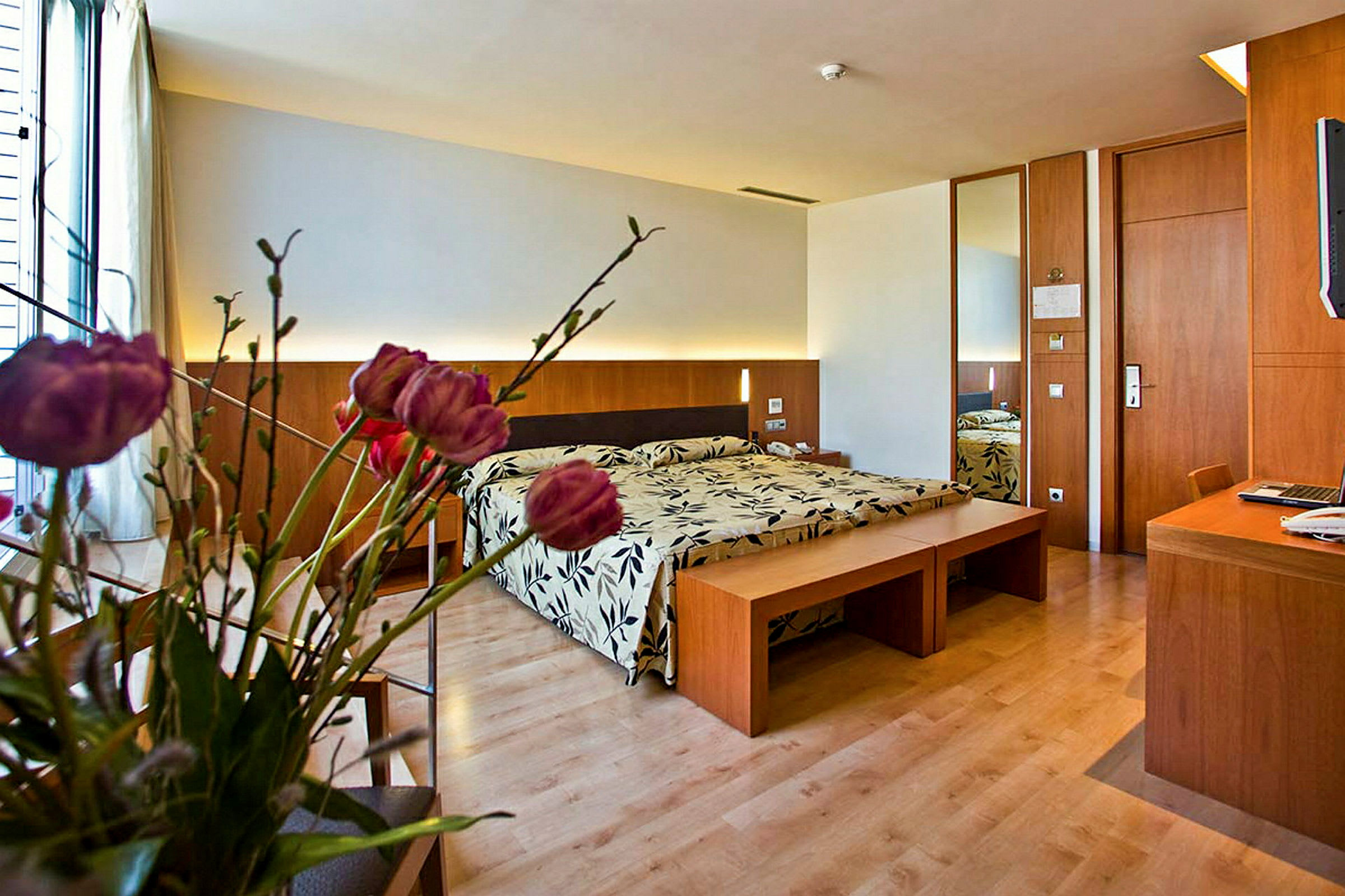 Ett modernt hotellrum med en säng, träinredning och en bukett blommor i förgrunden. (AI-genererad text)