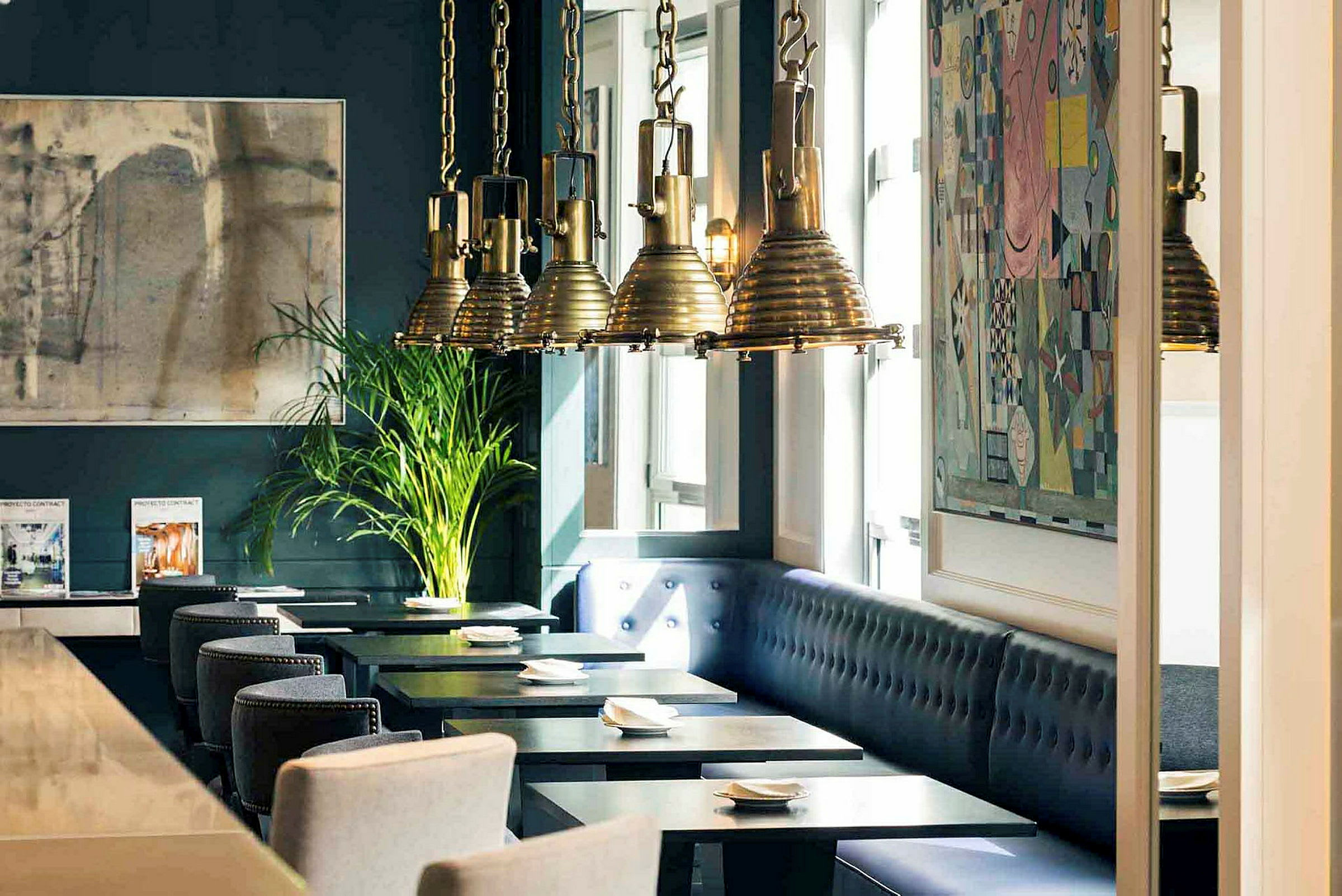 Interiör av en restaurang med mörkblåa väggar, konstverk, hängande lampor och sittplatser vid bord. (AI-genererad text)