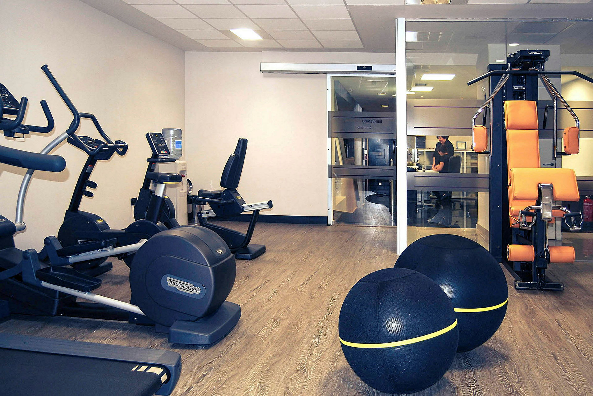 Ett gym med träningsmaskiner, två stora träningsbollar och en vattenautomat. (AI-genererad text)