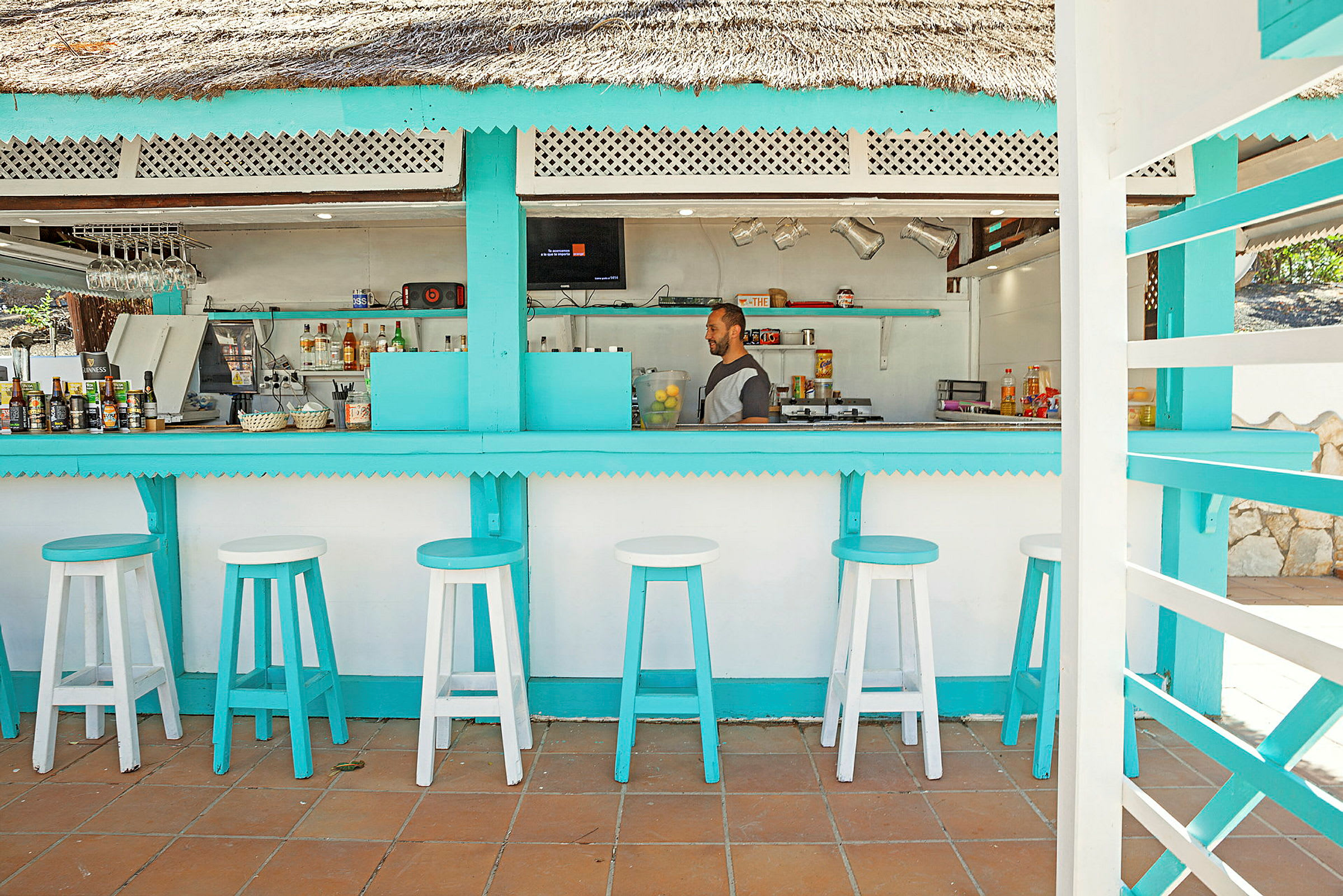 En strandbar med turkosa detaljer och vita barstolar. (AI-genererad text)