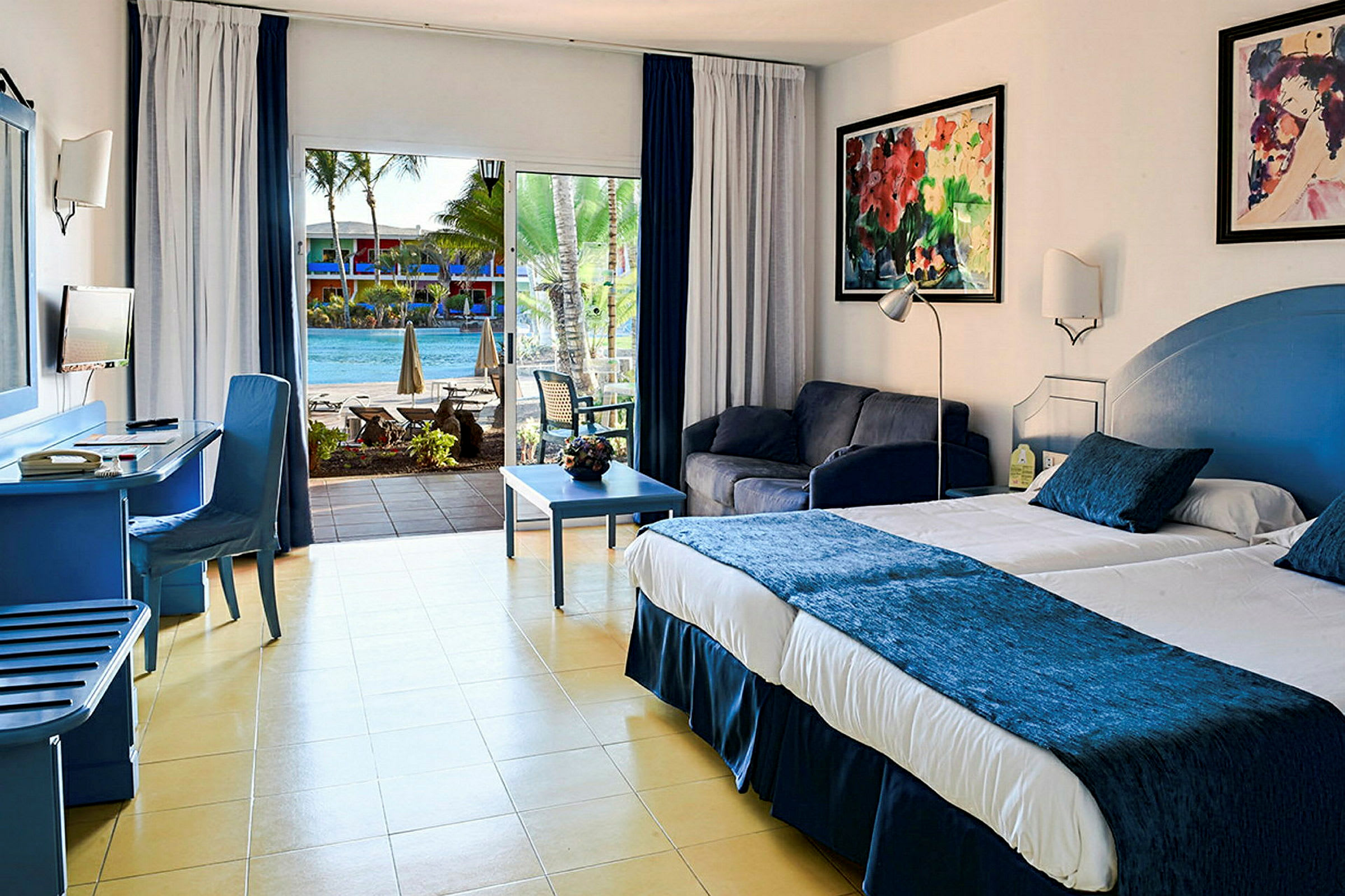 Ett hotellrum med en stor säng, sittgrupp och utsikt över en pool genom glasdörrar. (AI-genererad text)