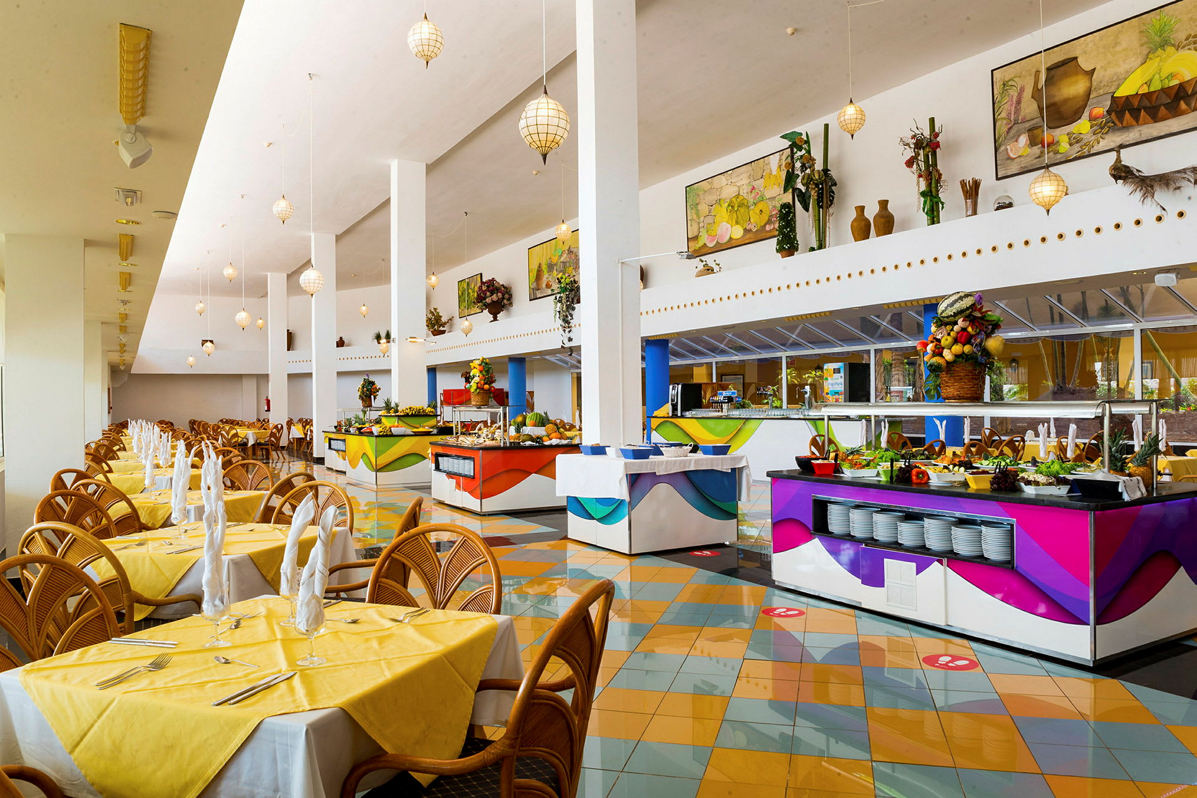 En rymlig restaurang med luftiga lokaler, gula dukar på borden och flera färgglada bufféstationer. (AI-genererad text)