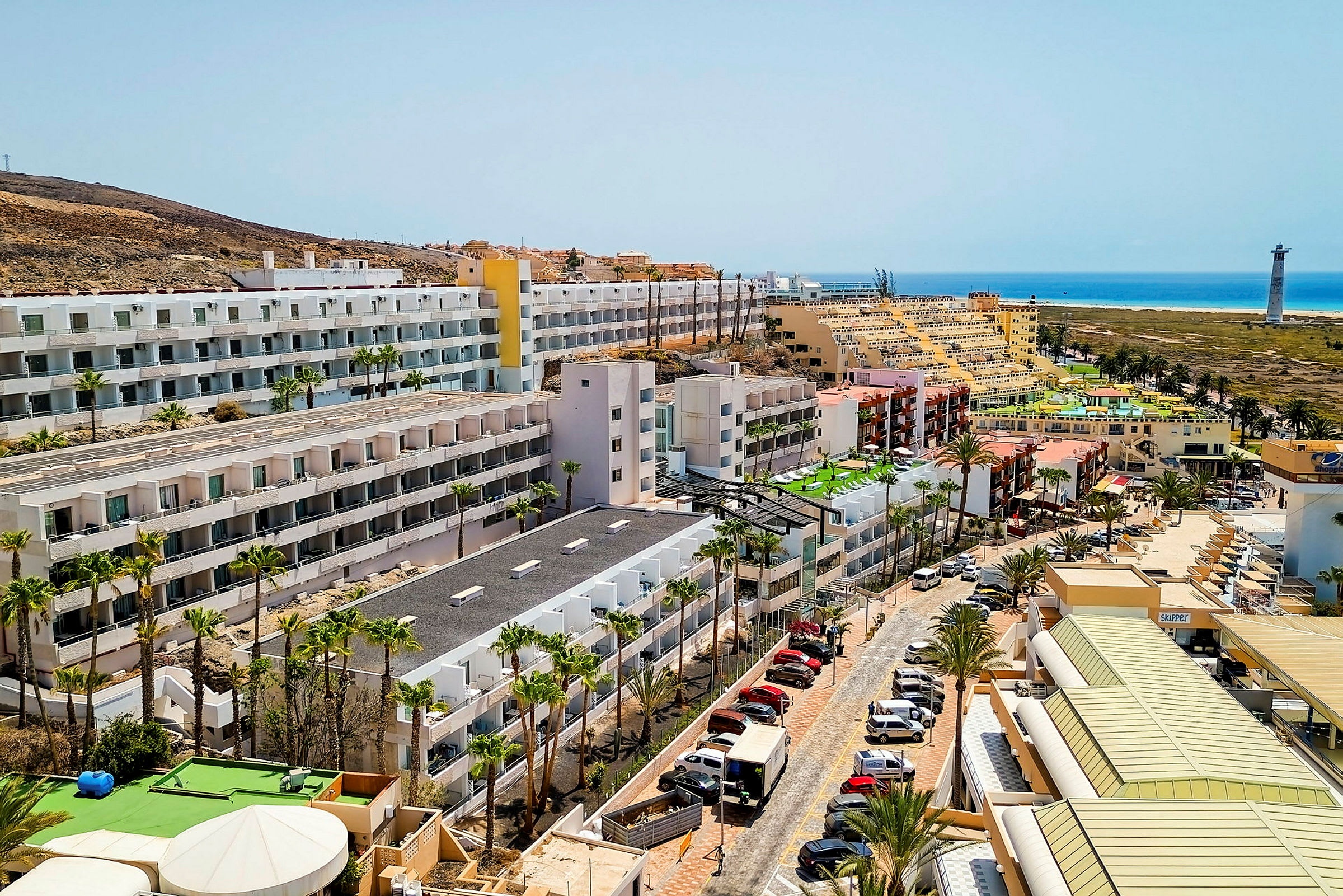 Hotellbyggnader nära havet med parkerade bilar och palmer. (AI-genererad text)