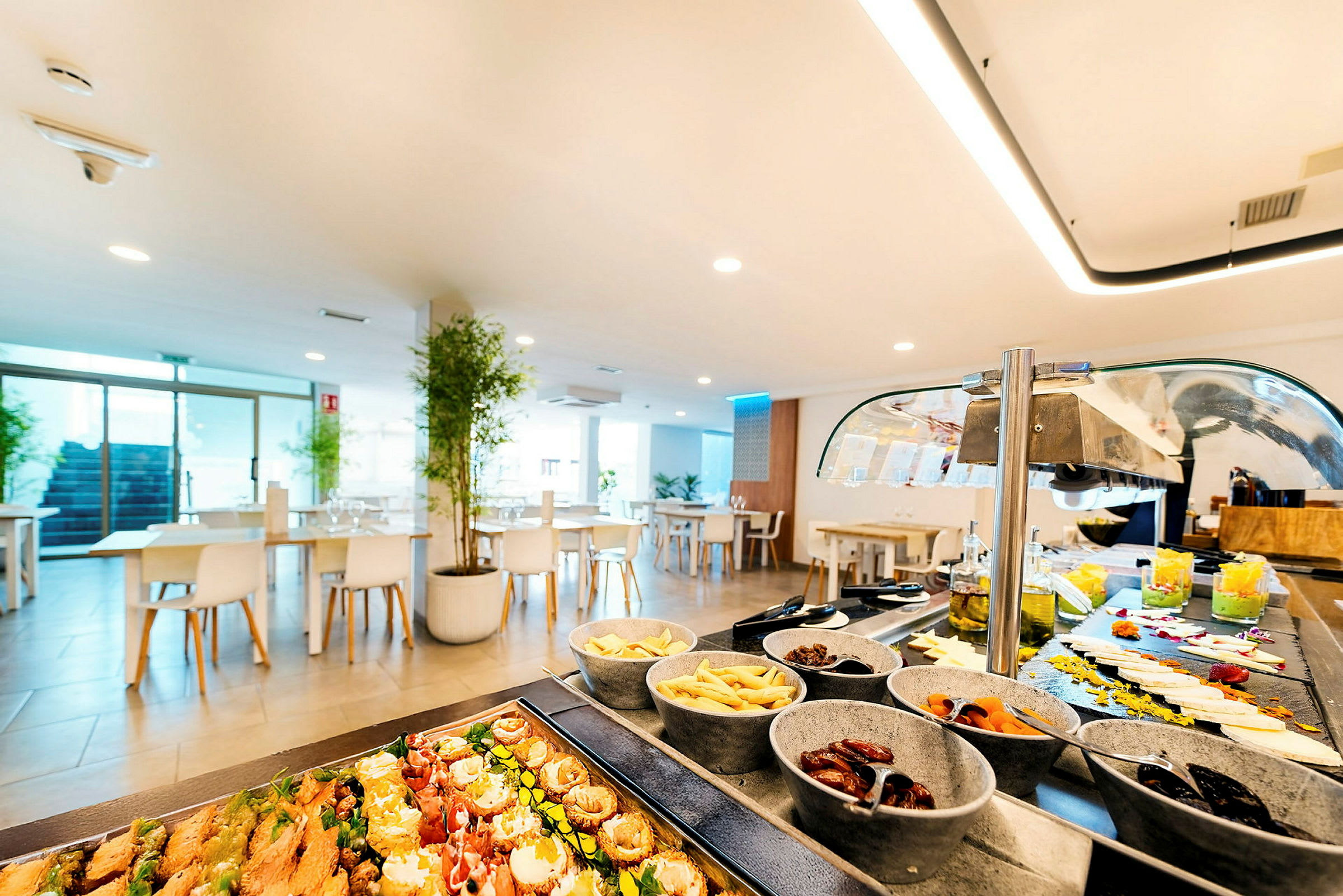 En ljus restaurang interiör med buffébord fylld med olika rätter och små skålar. (AI-genererad text)