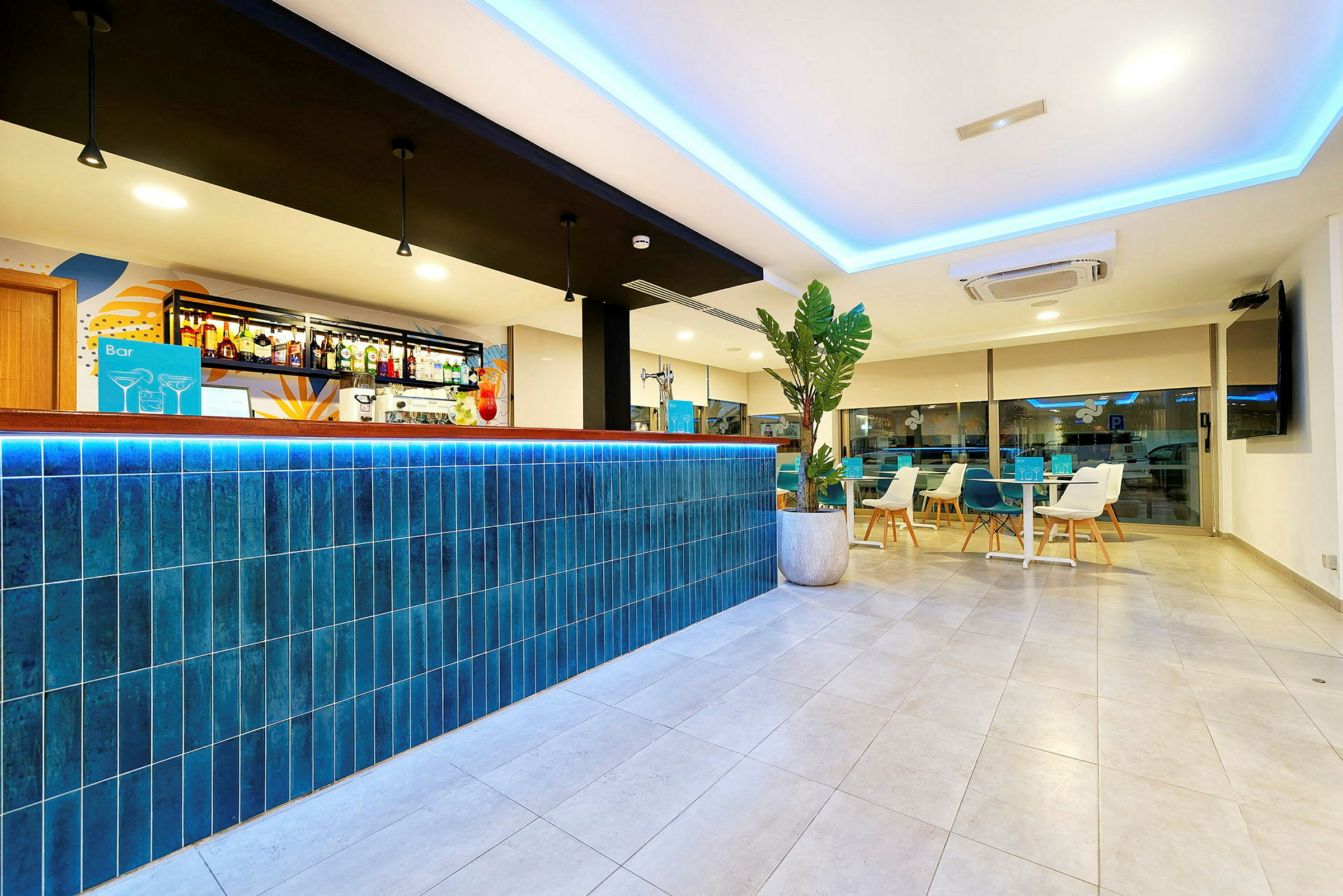 En modern hotellbar med en blå kaklad bardisk och stilren inredning. I bakgrunden syns sittgrupper och en stor fönstervägg. (AI-genererad text)
