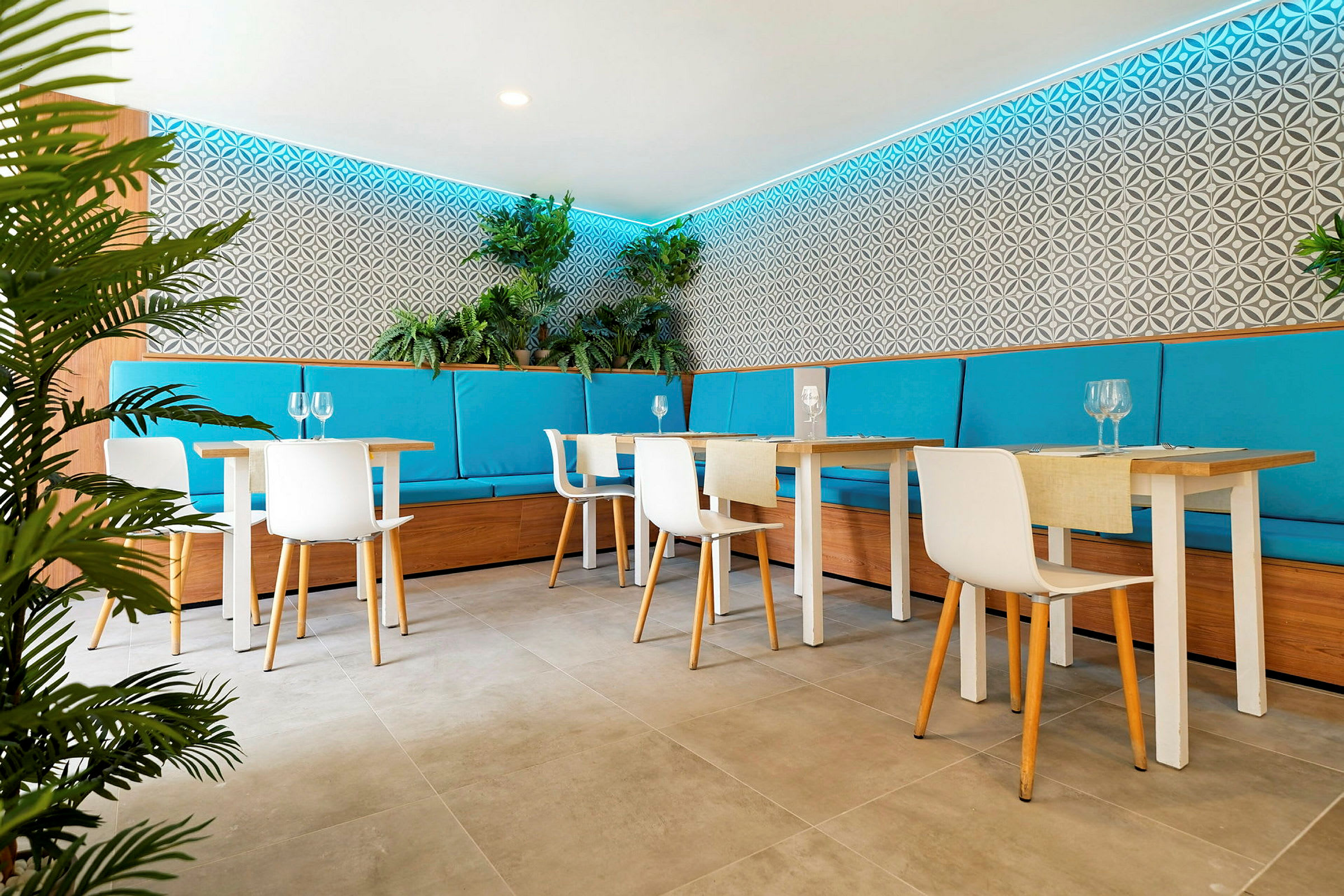 En modern restaurang med ljusa möbler, turkosa sittdynor och växter som dekoration längs väggarna. (AI-genererad text)