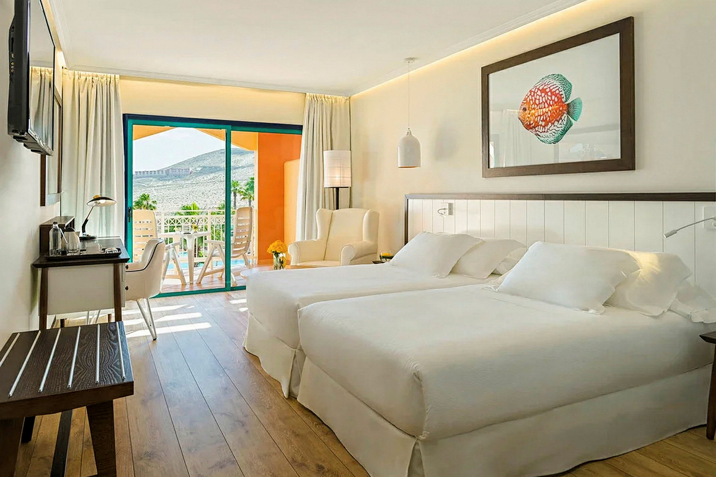 Ett ljust och modernt hotellrum med två sängar, en sittgrupp och ett skrivbord. En balkong med utsikt över landskapet syns i bakgrunden. (AI-genererad text)