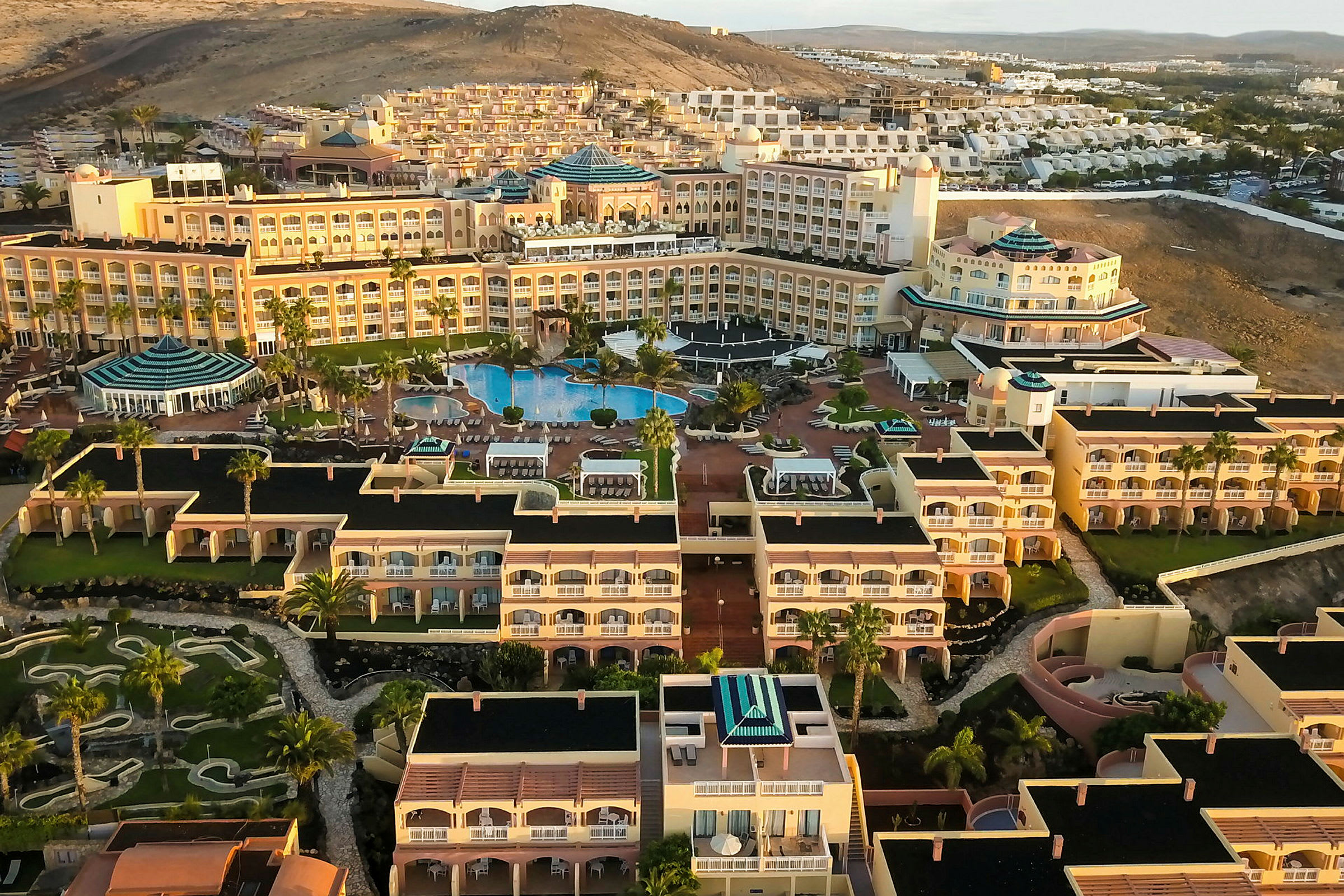 Flygfoto av en stor resort med poolområde, hotellbyggnader och landskap. (AI-genererad text)