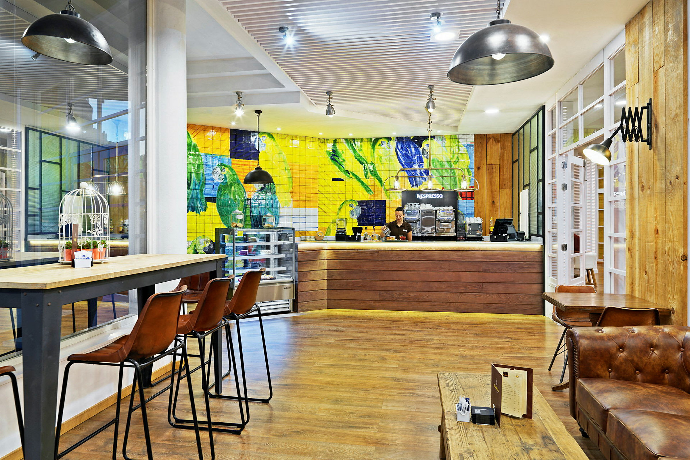 Interiören av ett kafé med färgglad kakelvägg, höga stolar och trädetaljer. (AI-genererad text)