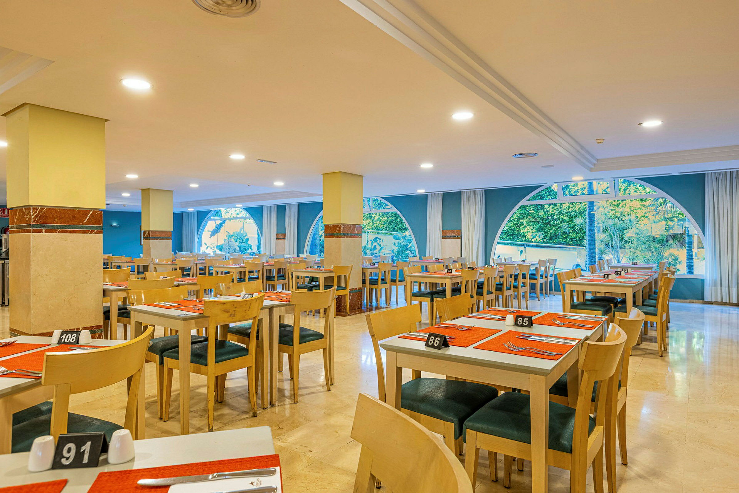 Interiör av en restaurang med dukade bord och stora fönster. (AI-genererad text)