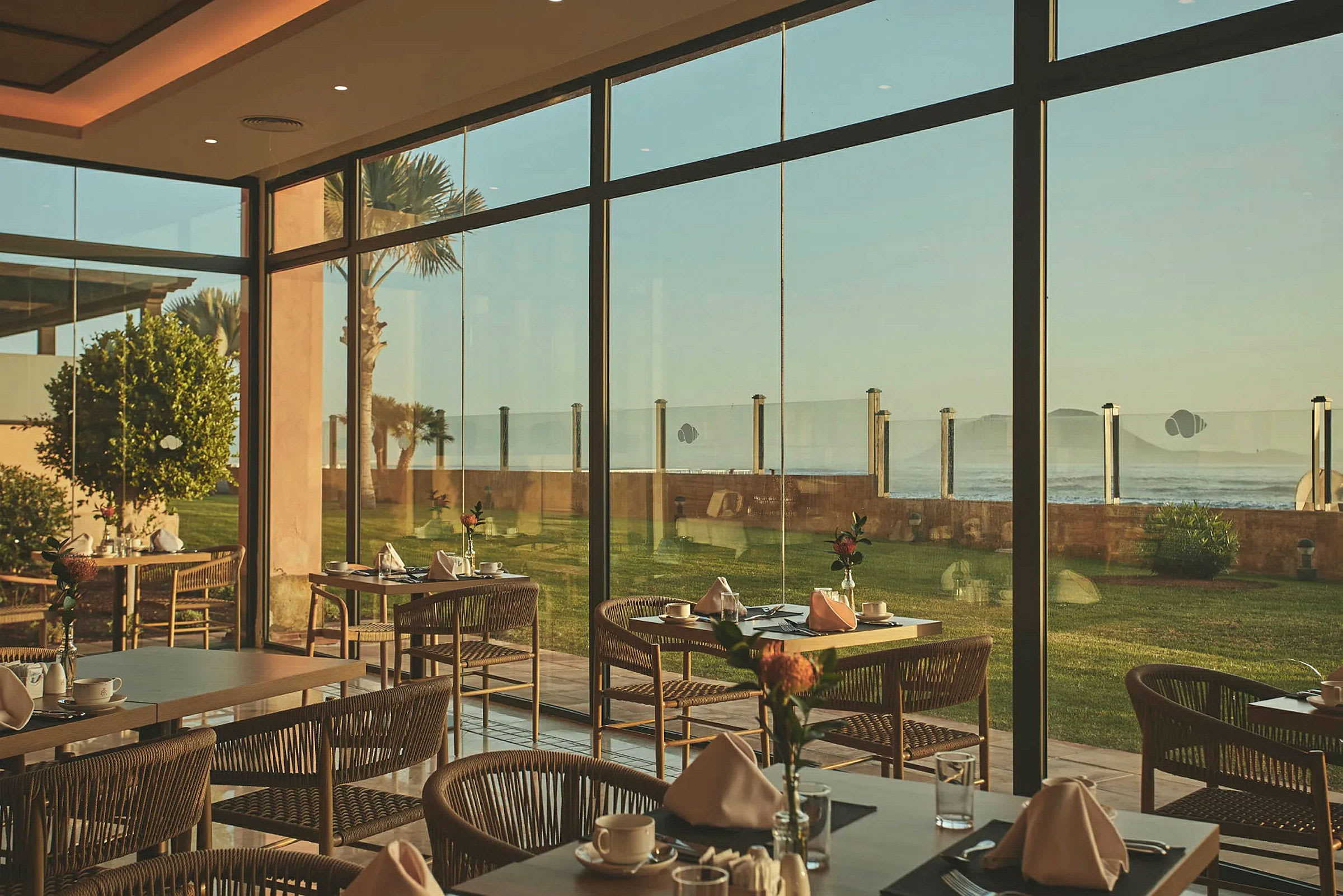 Restaurang med dukade bord och stora glasfönster med utsikt över havet. (AI-genererad text)