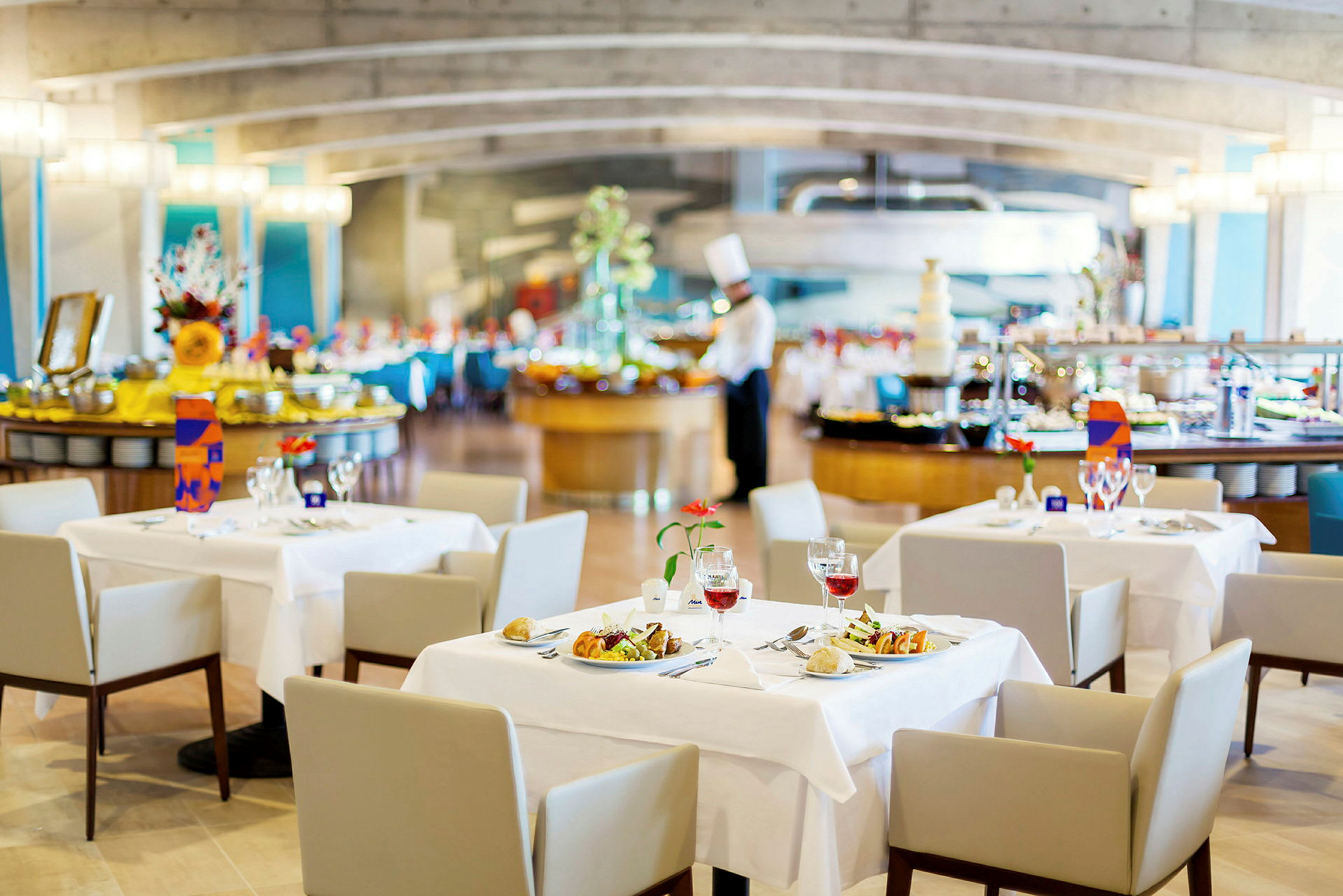 Restaurang med dukade bord, serveringsområde och en kock i bakgrunden. (AI-genererad text)