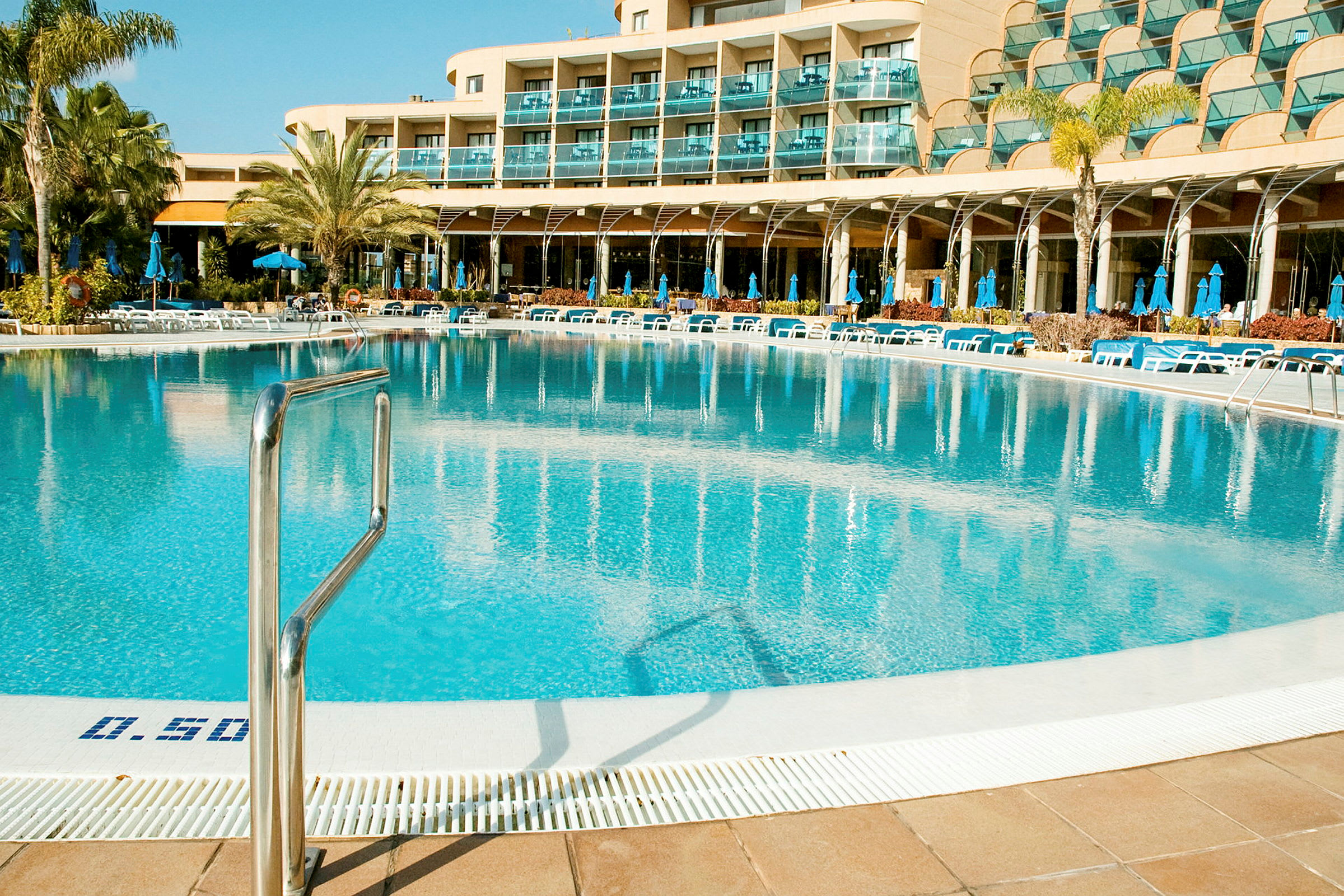 En stor pool omgiven av solstolar och parasoller vid ett hotell. (AI-genererad text)