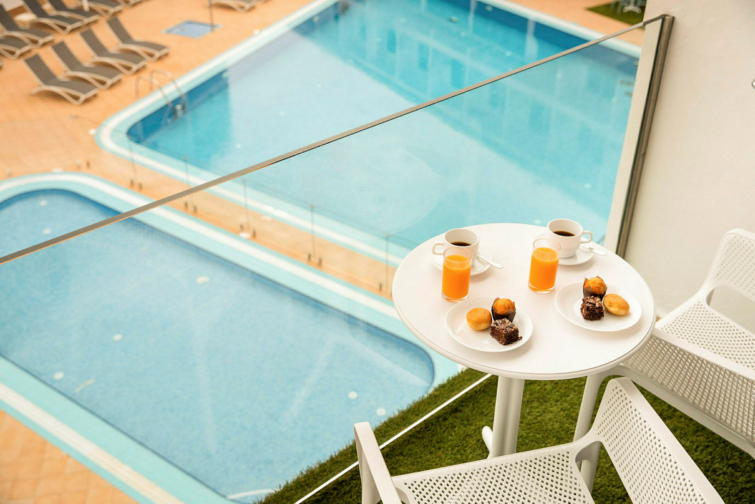 Bild av en balkong med två stolar och ett bord med frukost, inklusive kaffe och juice, samt en utsikt över en pool. (AI-genererad text)