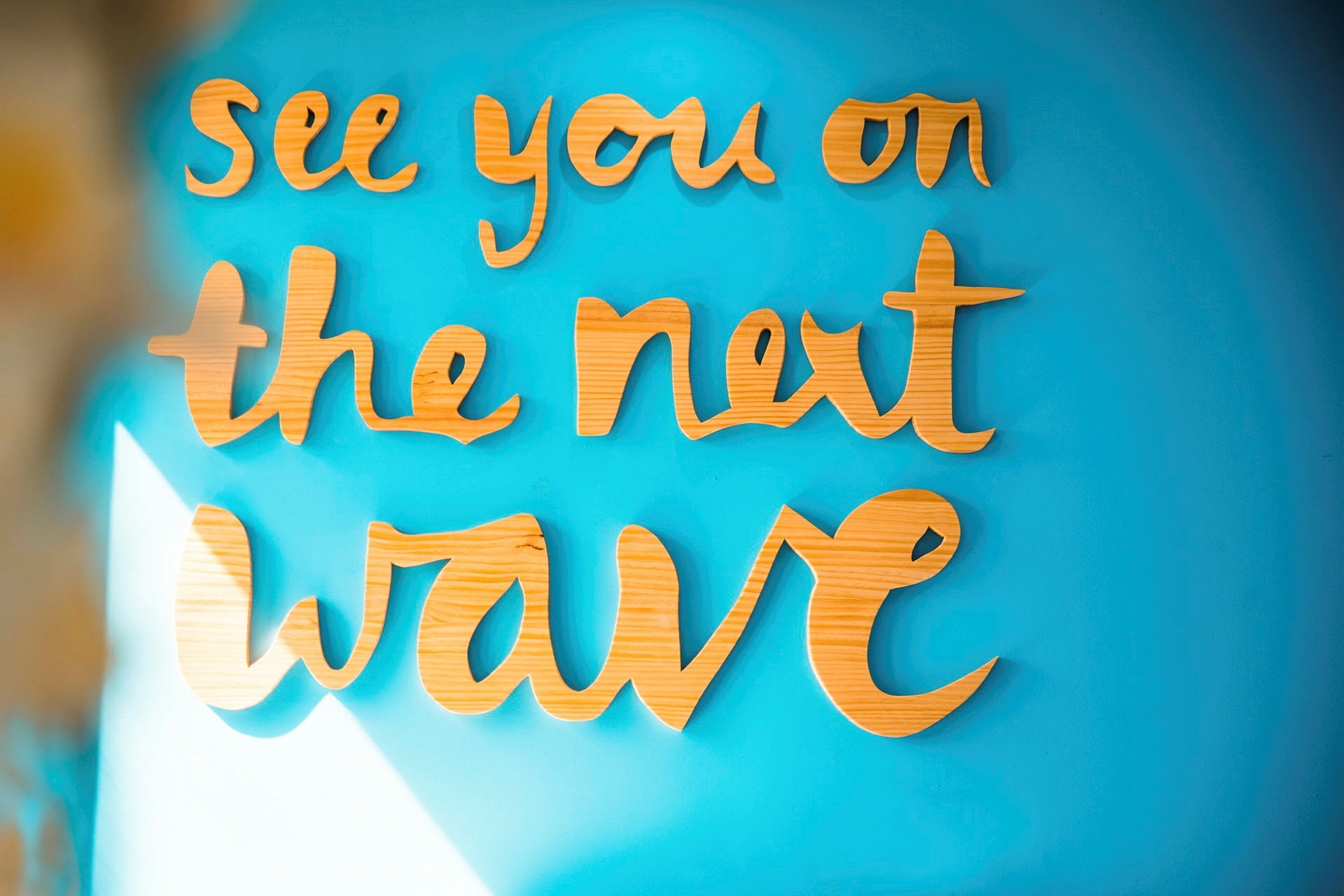 Text i trämaterial: "See you on the next wave" på en blå vägg. (AI-genererad text)