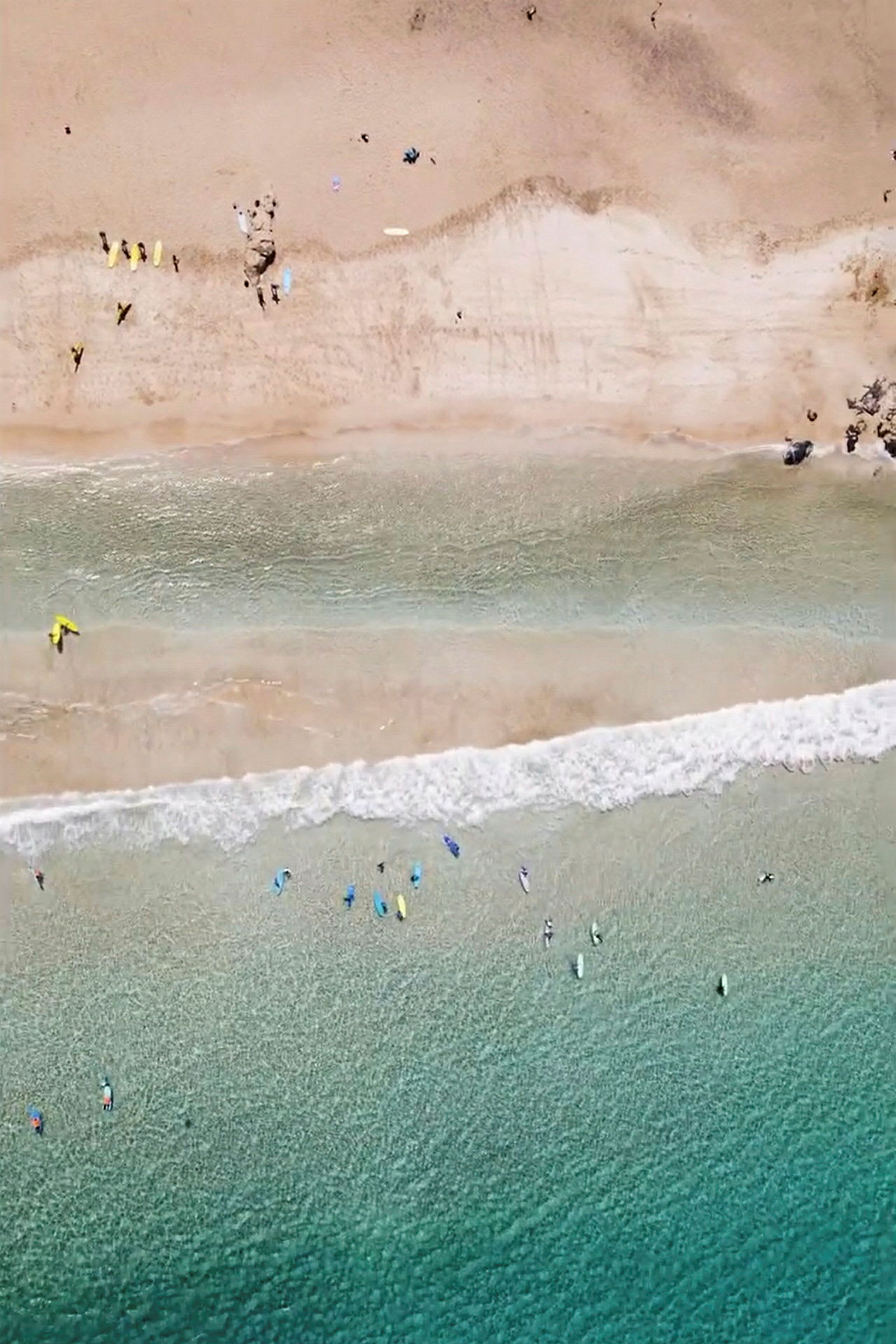 Flygbild av en strand med människor, vågor och surfbrädor i vattnet. (AI-genererad text)