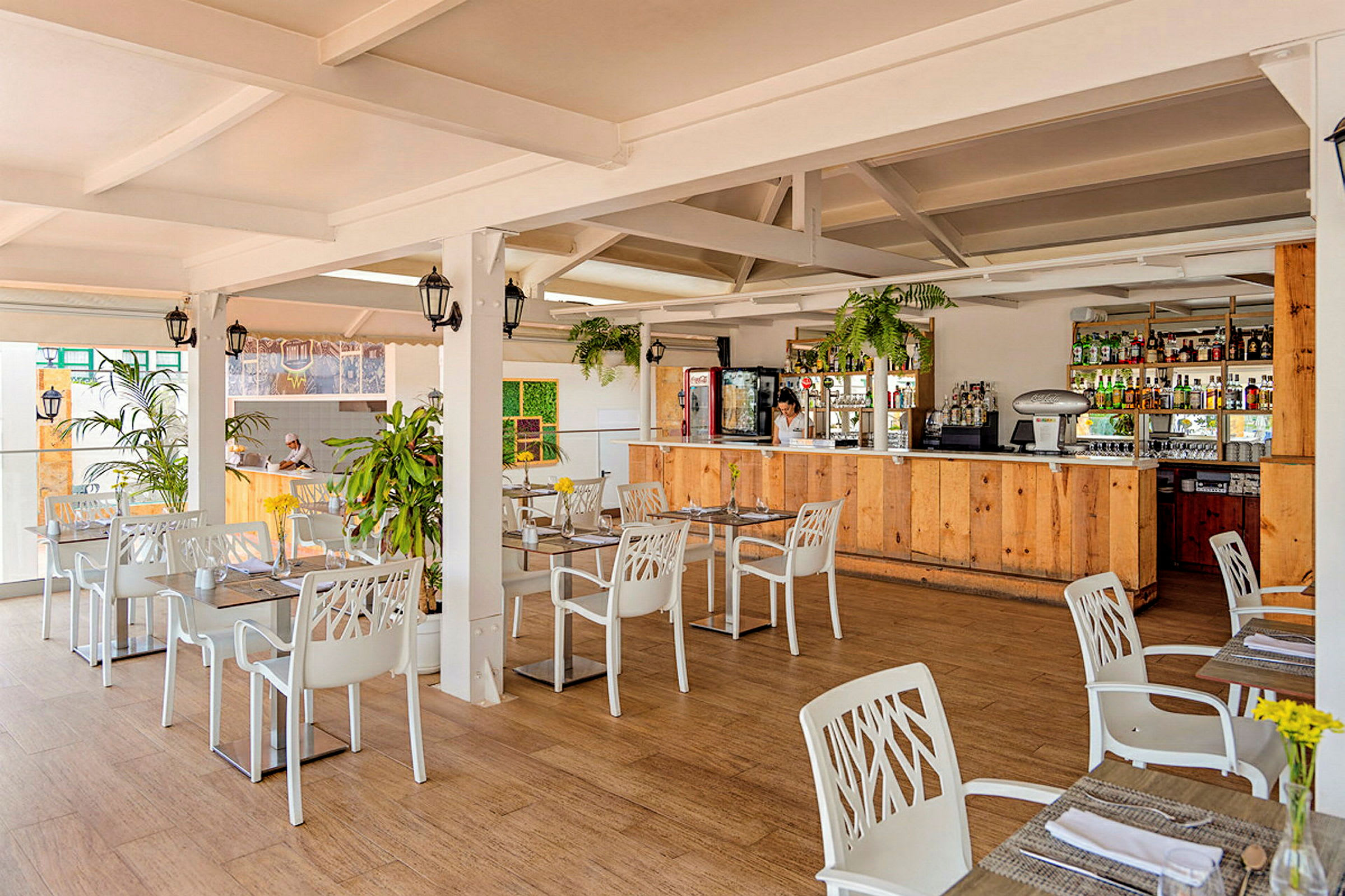 En ljus restaurang med vita bord och stolar samt en bardisk i trä. (AI-genererad text)