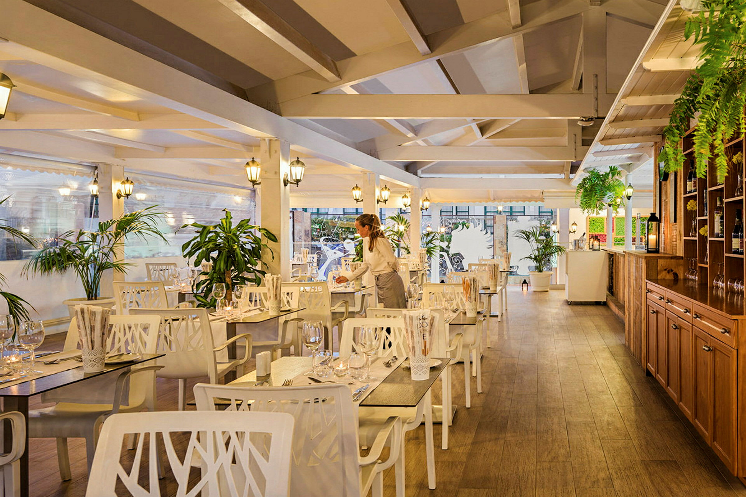Interiör av en restaurang med trädetaljer, vita möbler och gröna växter. (AI-genererad text)