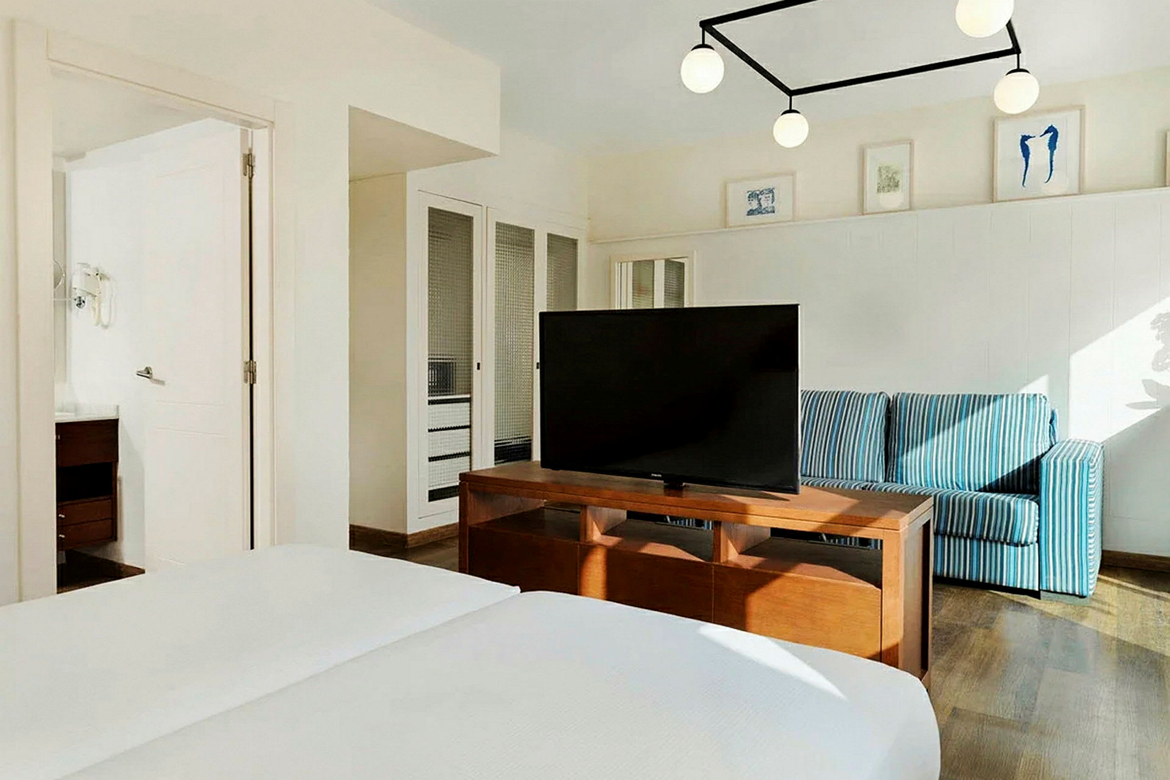 Ett hotellrum med en dubbelsäng, en tv på ett träbord, en blå randig soffa och väggdekorationer. (AI-genererad text)