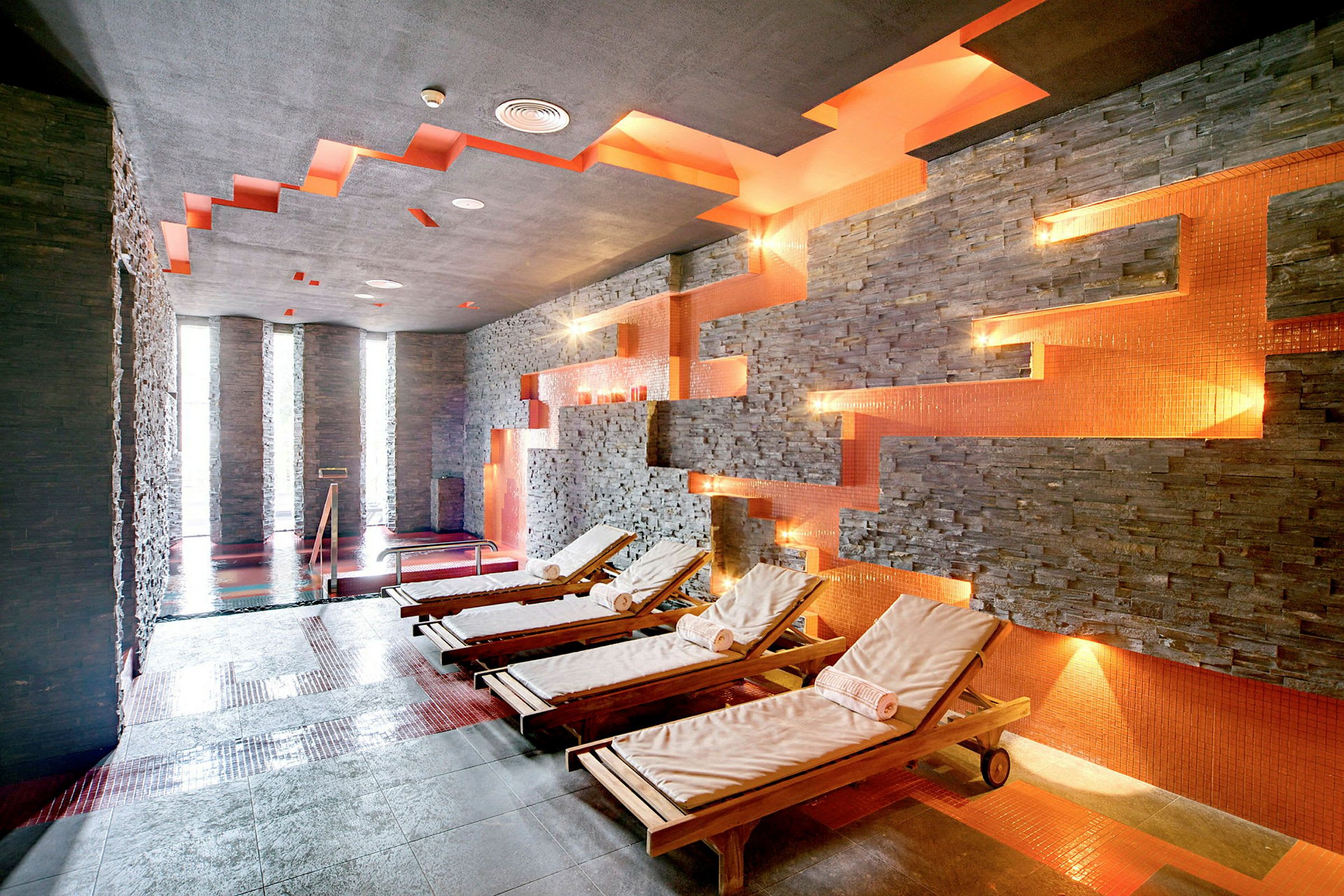 Ett spa med vilstolar i trä, stenväggar och orange belysning. (AI-genererad text)