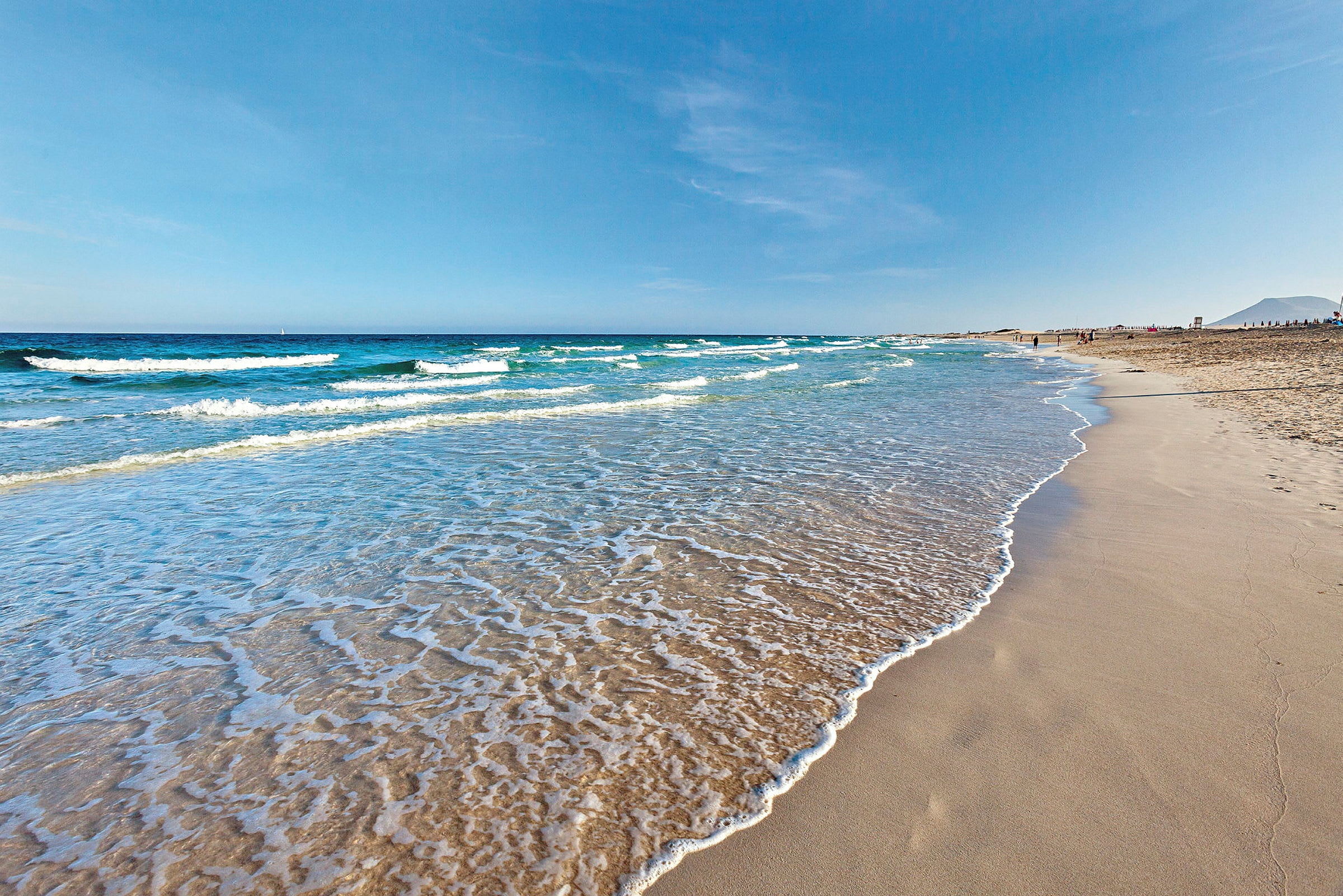 En sandstrand med mjuka vågor som sköljer in, under en klar blå himmel. (AI-genererad text)