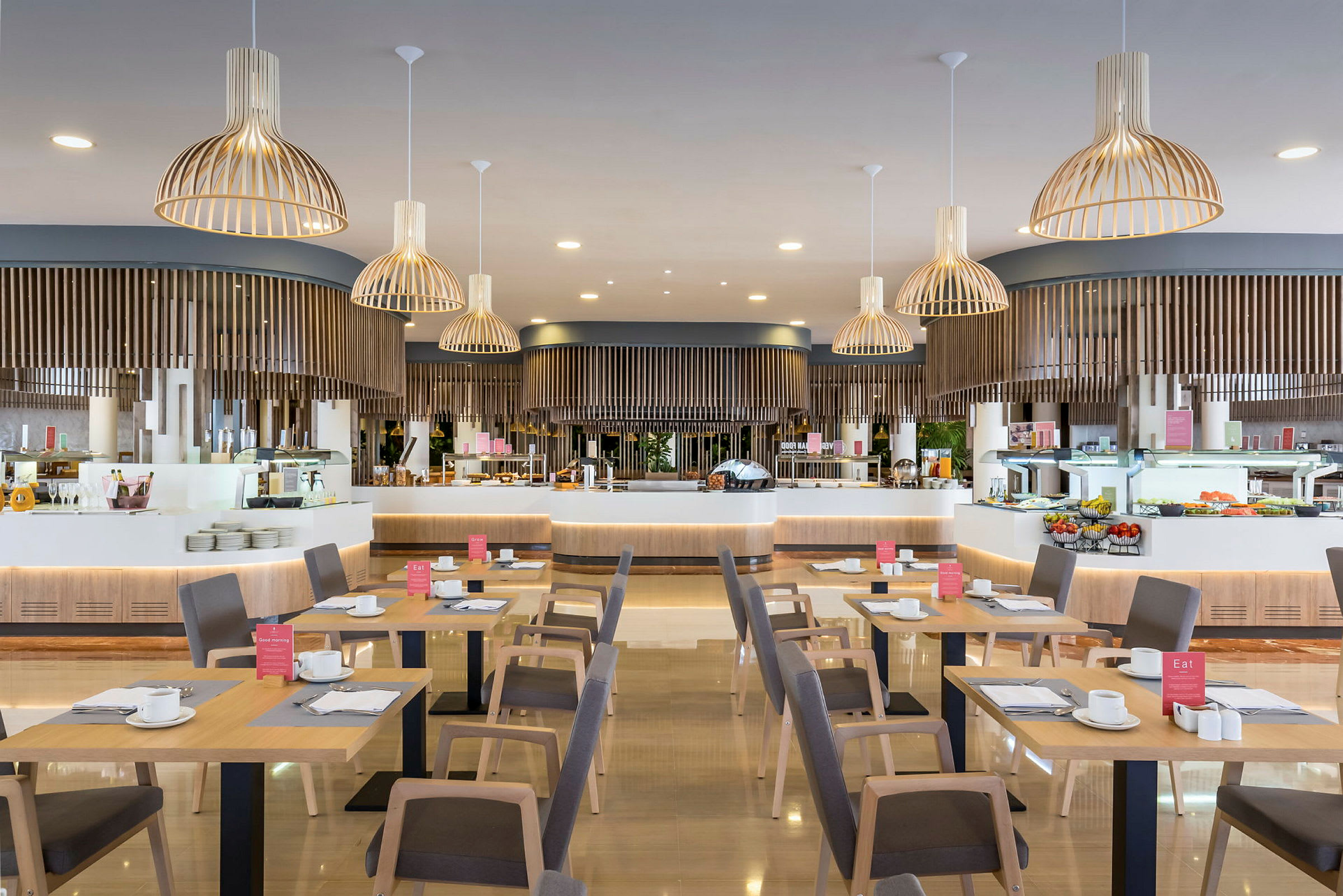 En restaurang med träbord och stolar, serveringsområde i bakgrunden med lampor hängande från taket. (AI-genererad text)