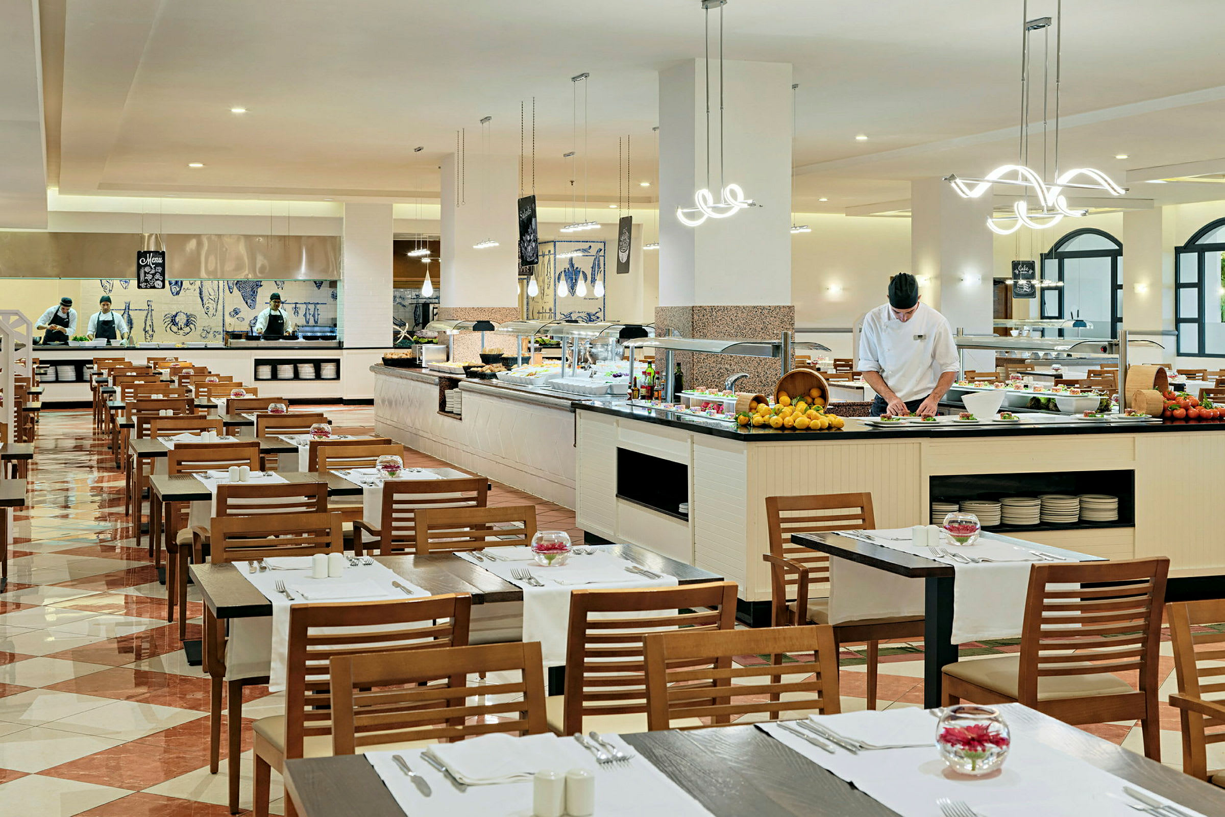 Restaurang med dukade bord och en buffé. Personal arbetar vid matstationen. (AI-genererad text)