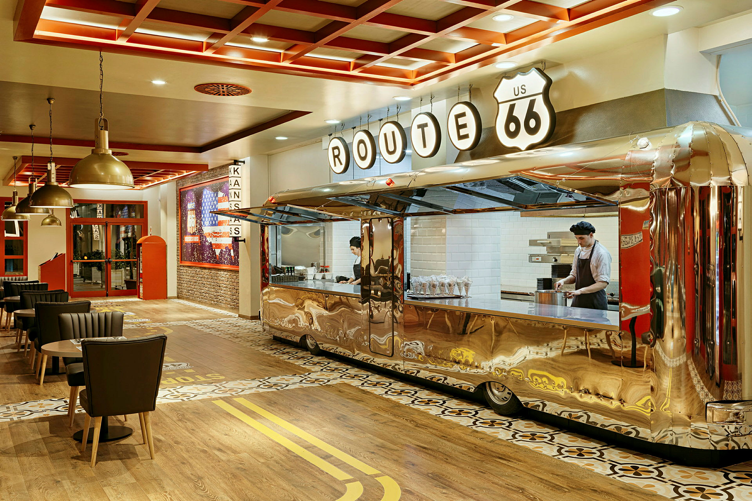 En interiör av en restaurang med ett retrotema, där en serveringsdisk är utformad som en glänsande trailer, och flera matbord samt stolar är placerade runt om. (AI-genererad text)