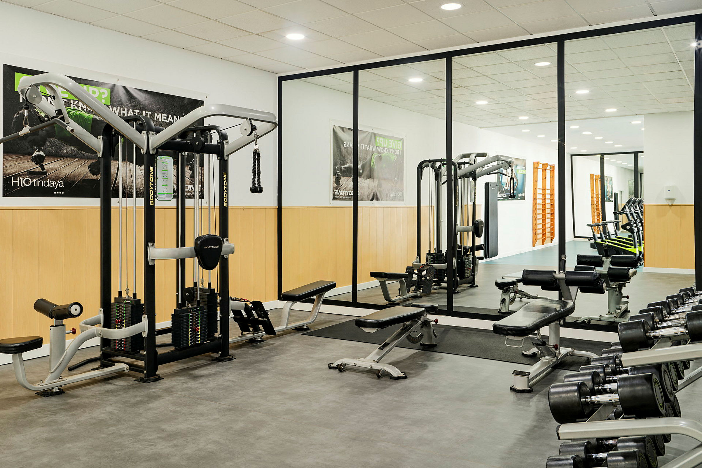 Ett gym med träningsutrustning, inklusive vikter, träningsbänkar och kabelmaskiner. Spegelväggar syns i bakgrunden. (AI-genererad text)