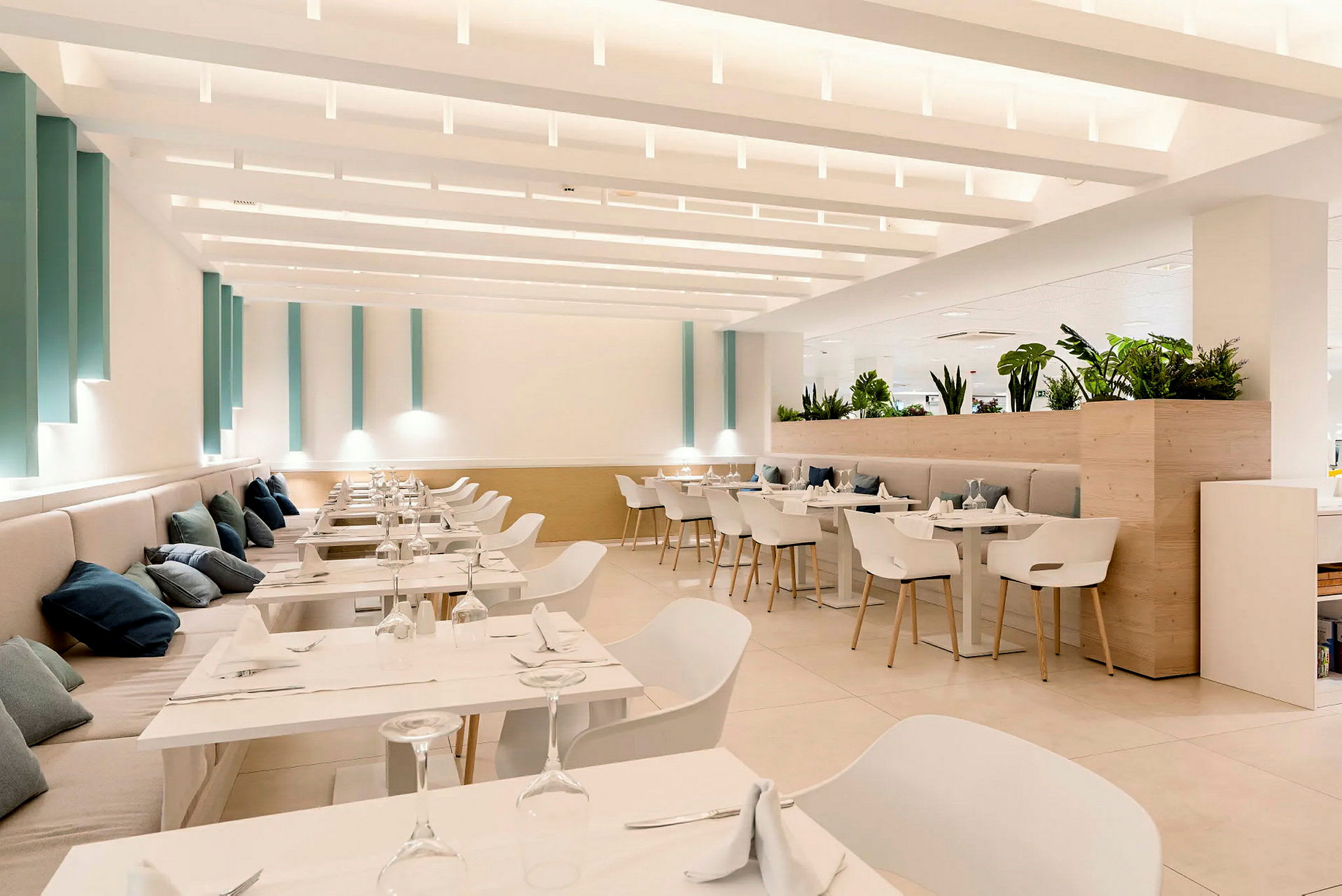 Ett ljust och modernt inrett restaurangområde med vita möbler och gröna växter. (AI-genererad text)