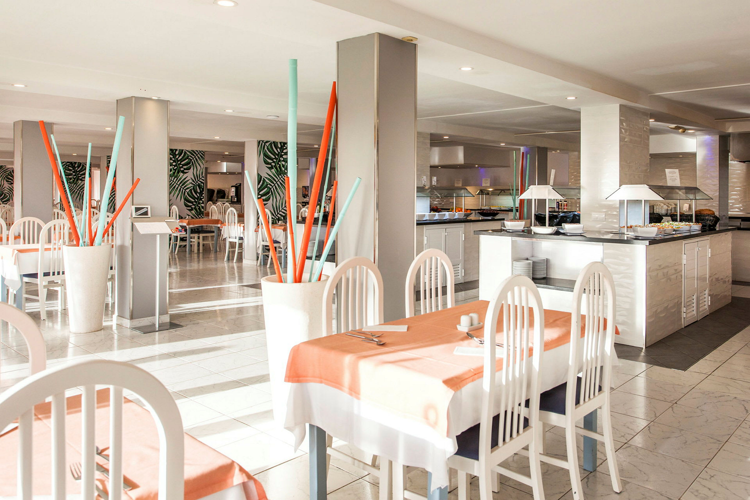 En restaurang med ljusa möbler, bord klädda med dukar, och dekorativa element som färgglada stånginstallationer. (AI-genererad text)