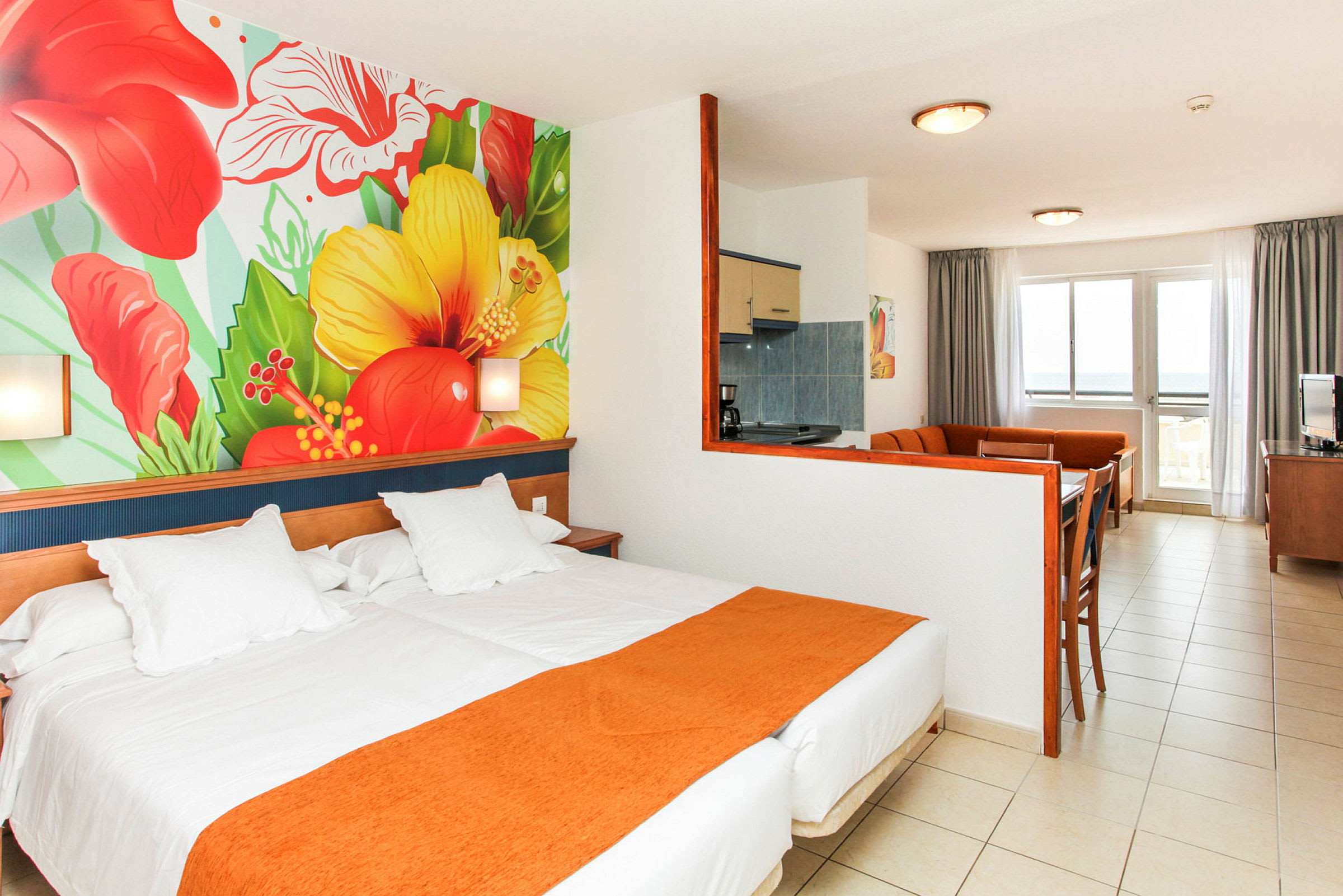 Hotellets rum med säng, färgglad väggmålning av blommor och sittgrupp med kök. (AI-genererad text)