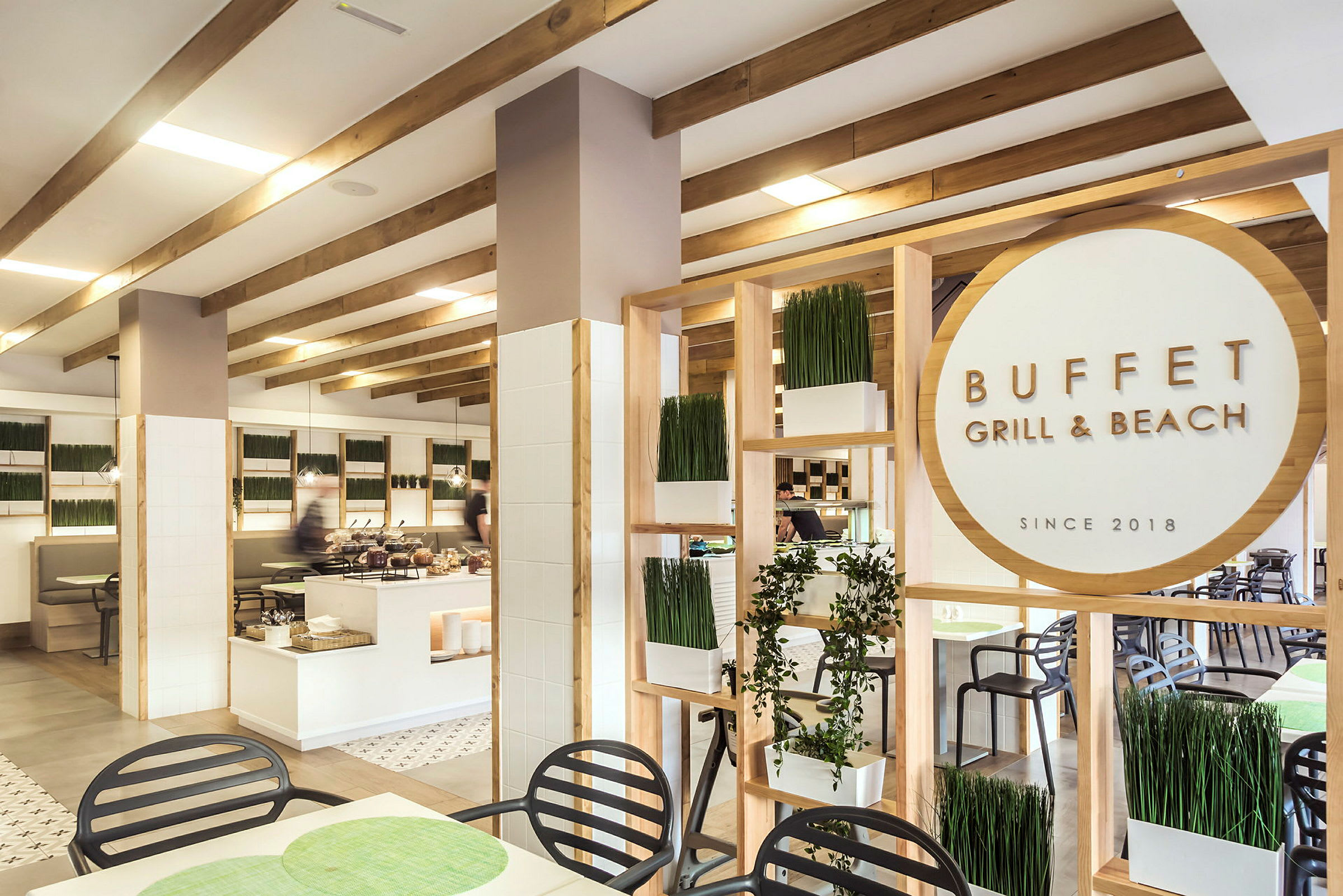 Interiör av en restaurang med buffé, med trädetaljer, växtdekorationer och en skylt med texten "Buffet Grill & Beach". (AI-genererad text)