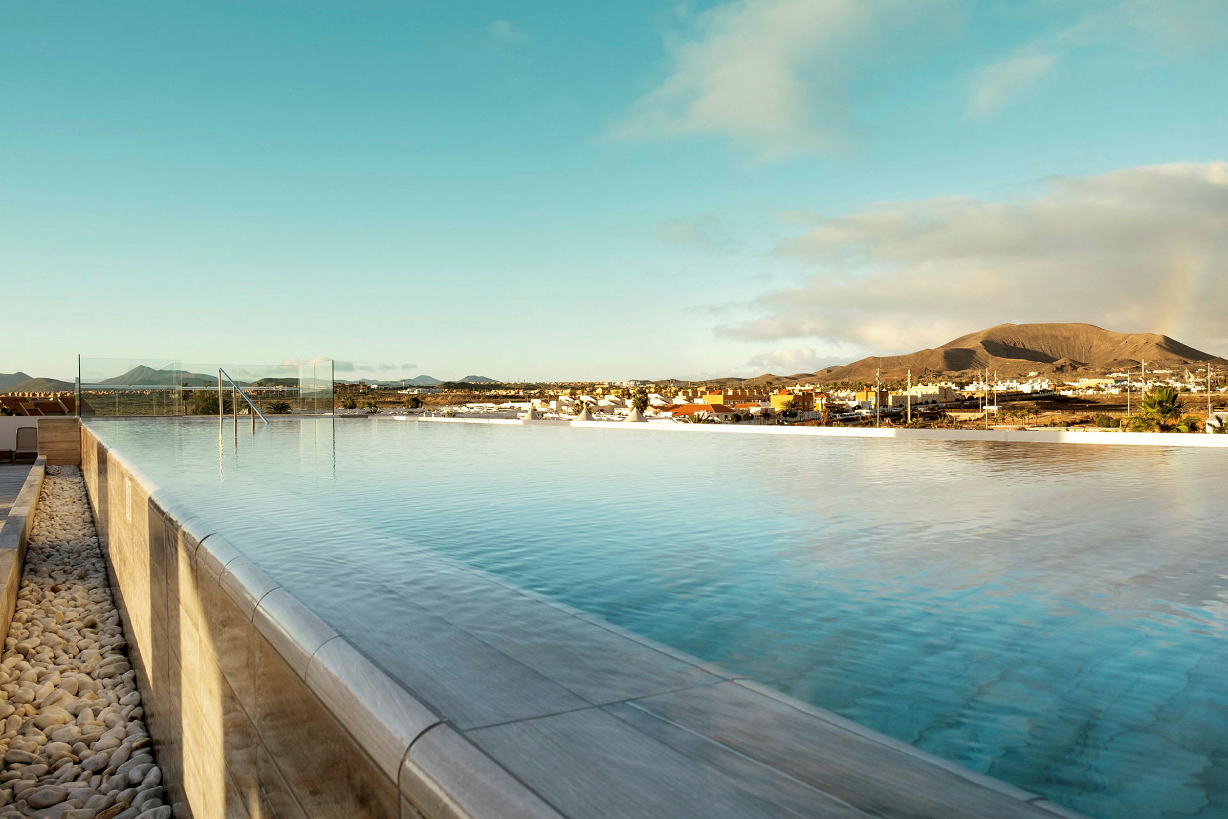 En infinitypool under klar himmel med utsikt över en stad och berg i bakgrunden. (AI-genererad text)