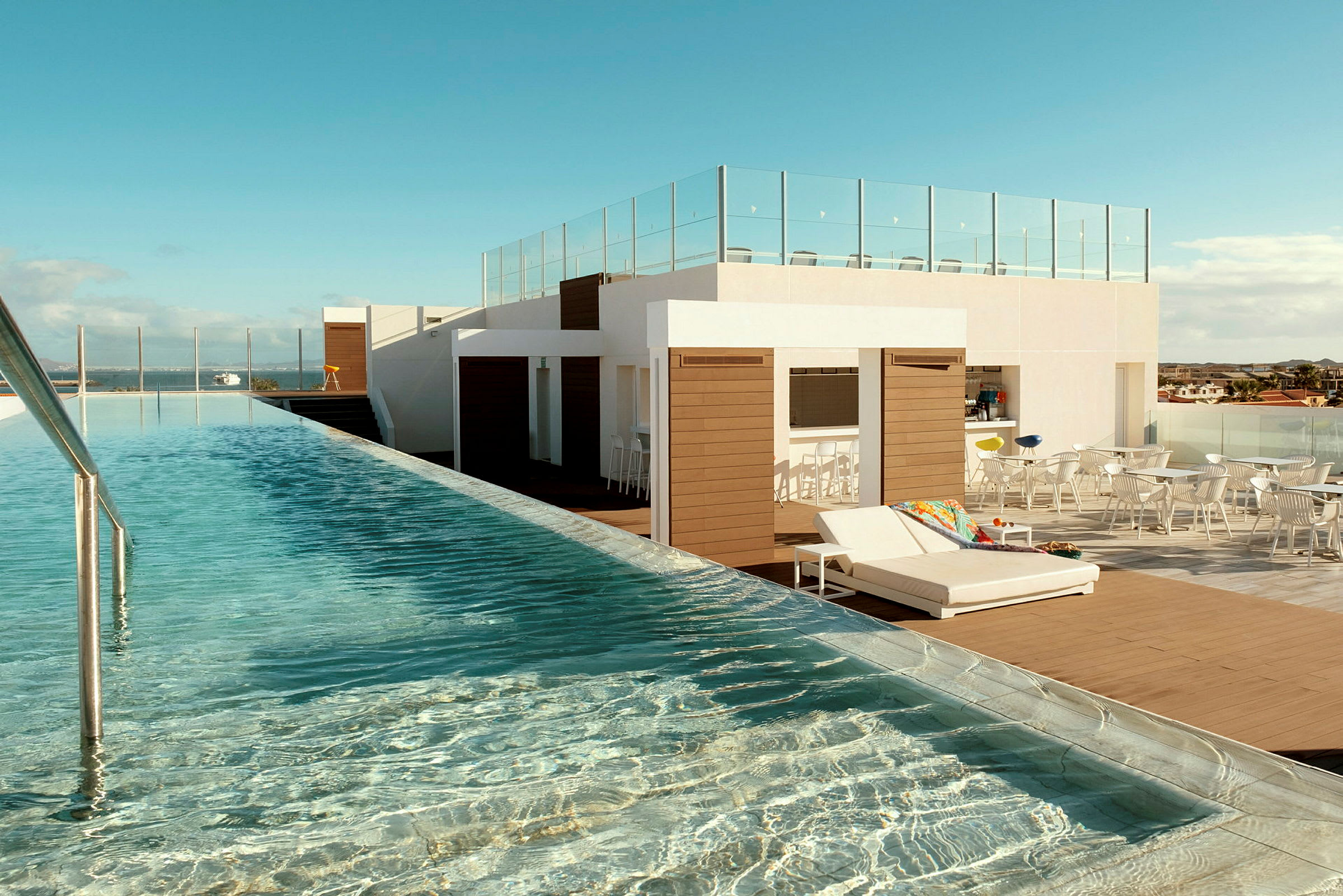 En takterrass med en lång infinitypool, solbäddar och loungemöbler under bar himmel. (AI-genererad text)