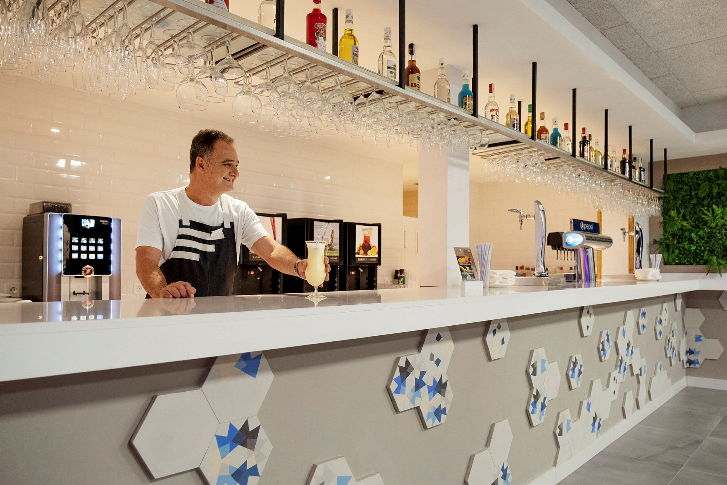 En bartender vid en modern bardisk med flaskor och glas upphängda ovanför. (AI-genererad text)