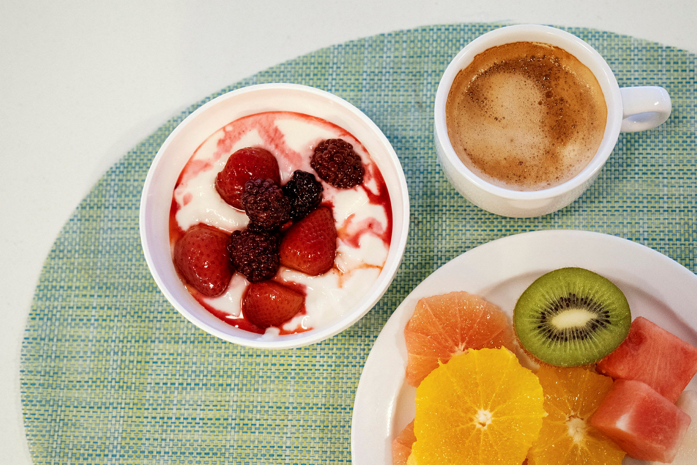 En frukost med yoghurt toppad med bär, en kopp kaffe och skivat färsk frukt. (AI-genererad text)