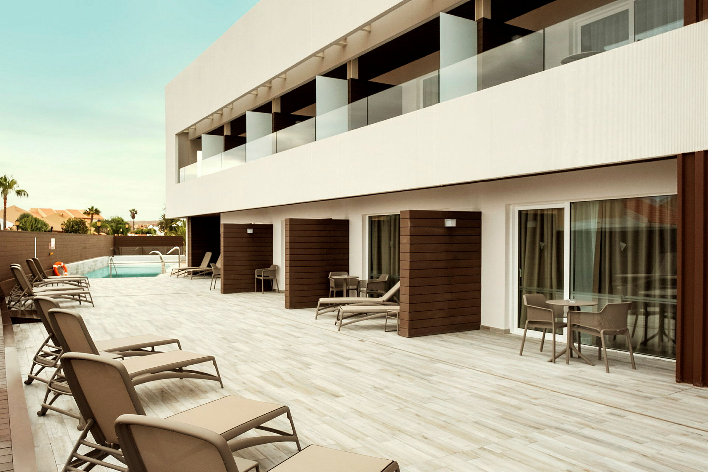 Hotellområde med terrassutrymme, solsängar och en pool i bakgrunden. (AI-genererad text)